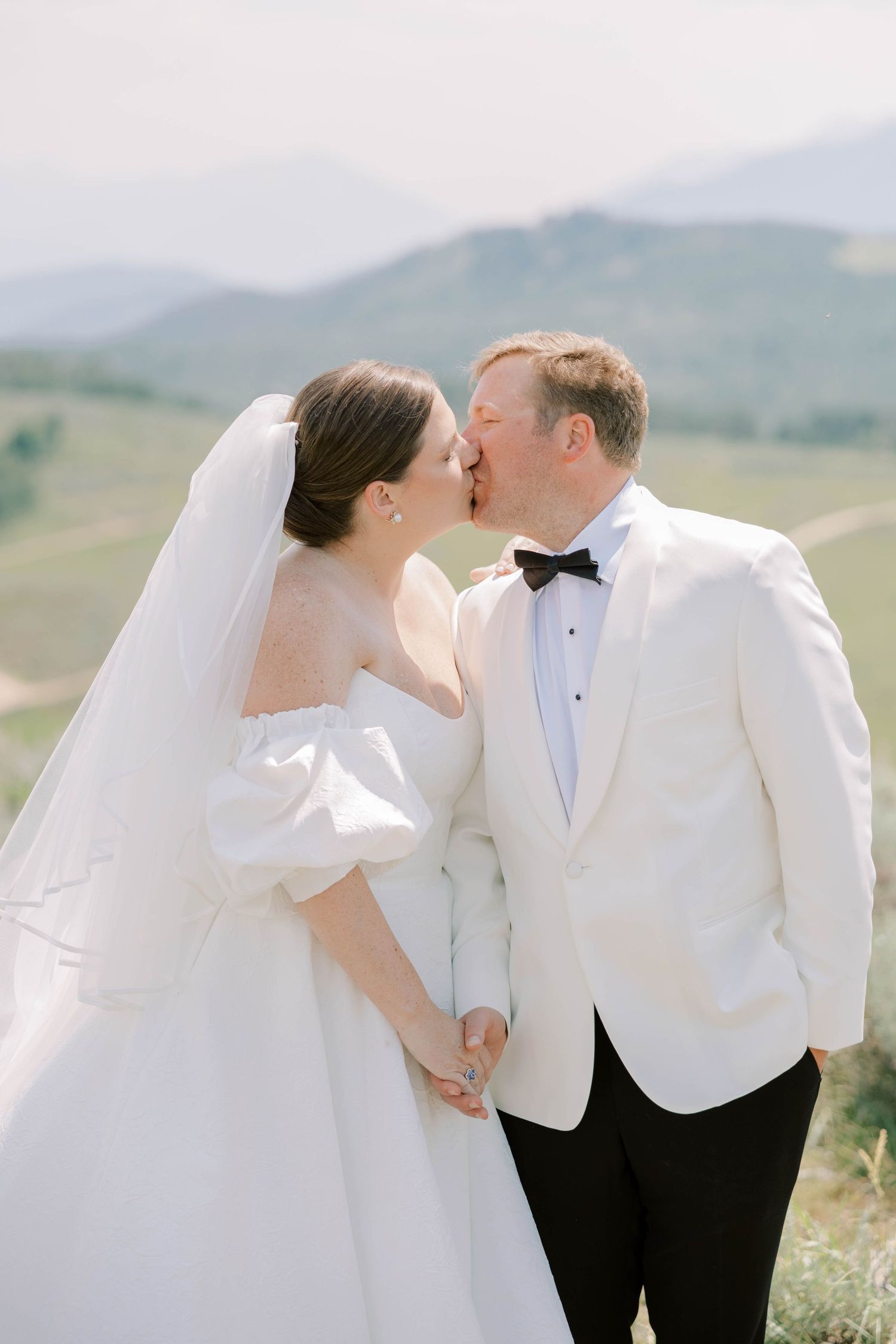 Newlyweds share an intimate moment against a backdrop of misty mountains in elegant white wedding attire.