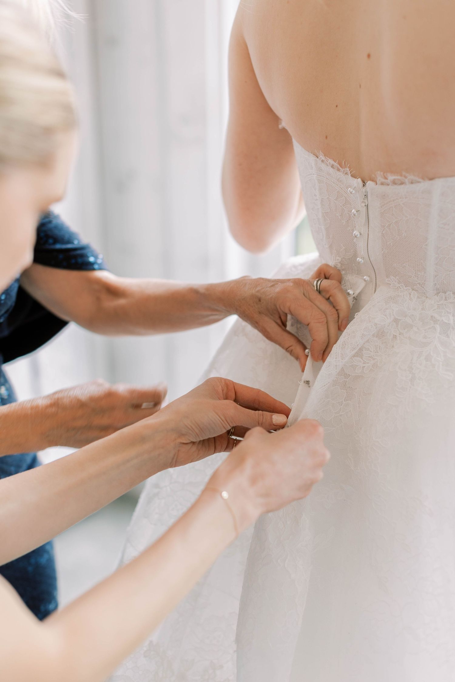 Close-up of hands adjusting and securing the back of an elegant white wedding dress.