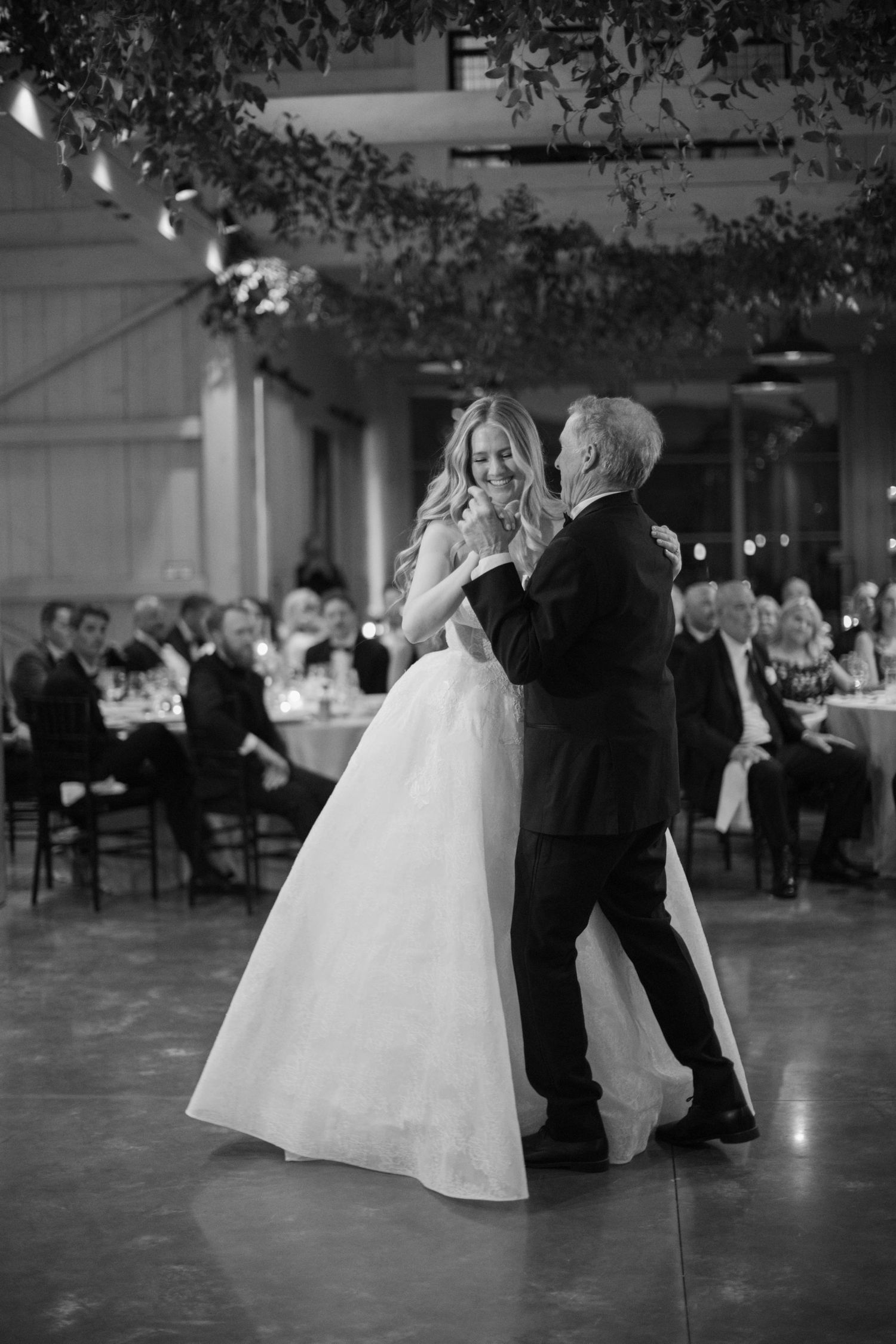 A couple shares their first dance in an elegant reception hall under hanging greenery.