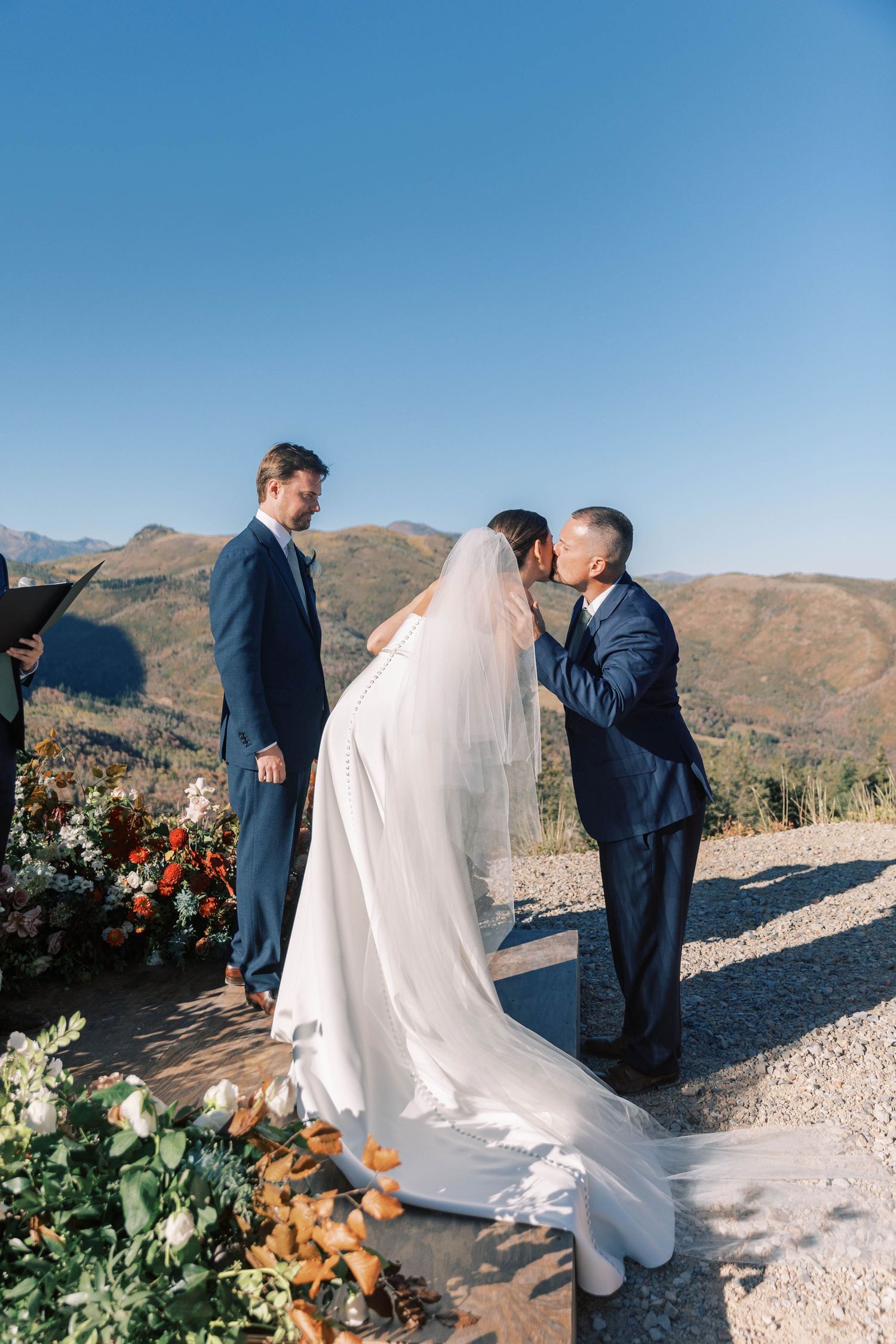 Mountain wedding ceremony with flowing white dress and floral decorations.