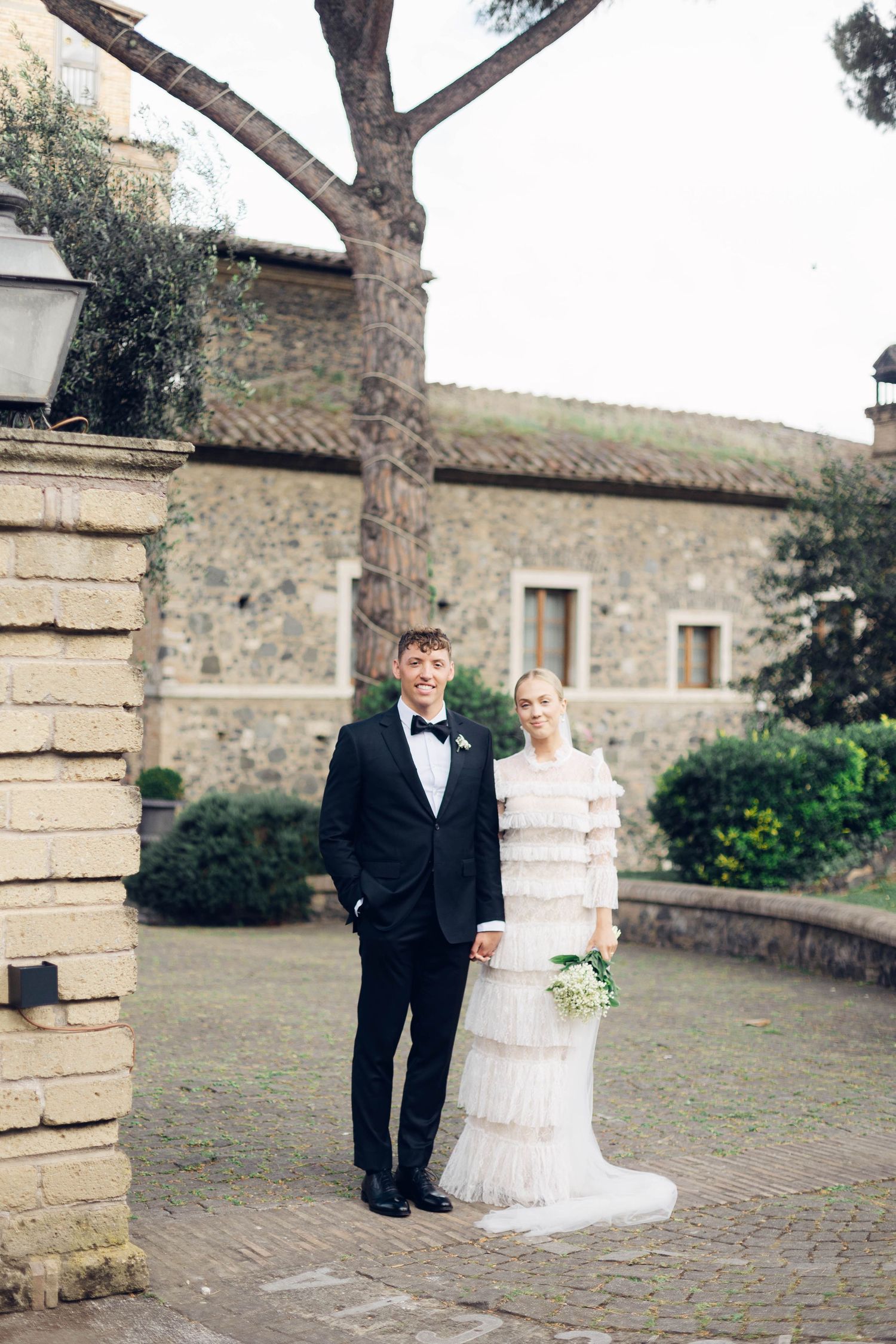 Elegant wedding couple poses against a rustic stone building backdrop in Italy at castello della castellucia.