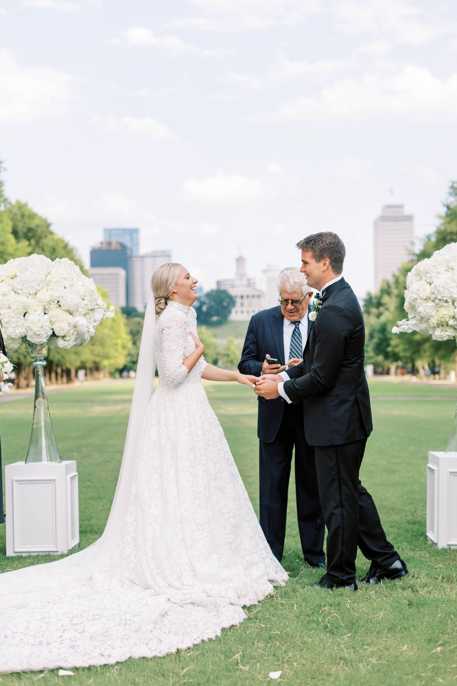 Outdoor wedding ceremony setup with white floral arrangements and city skyline backdrop.