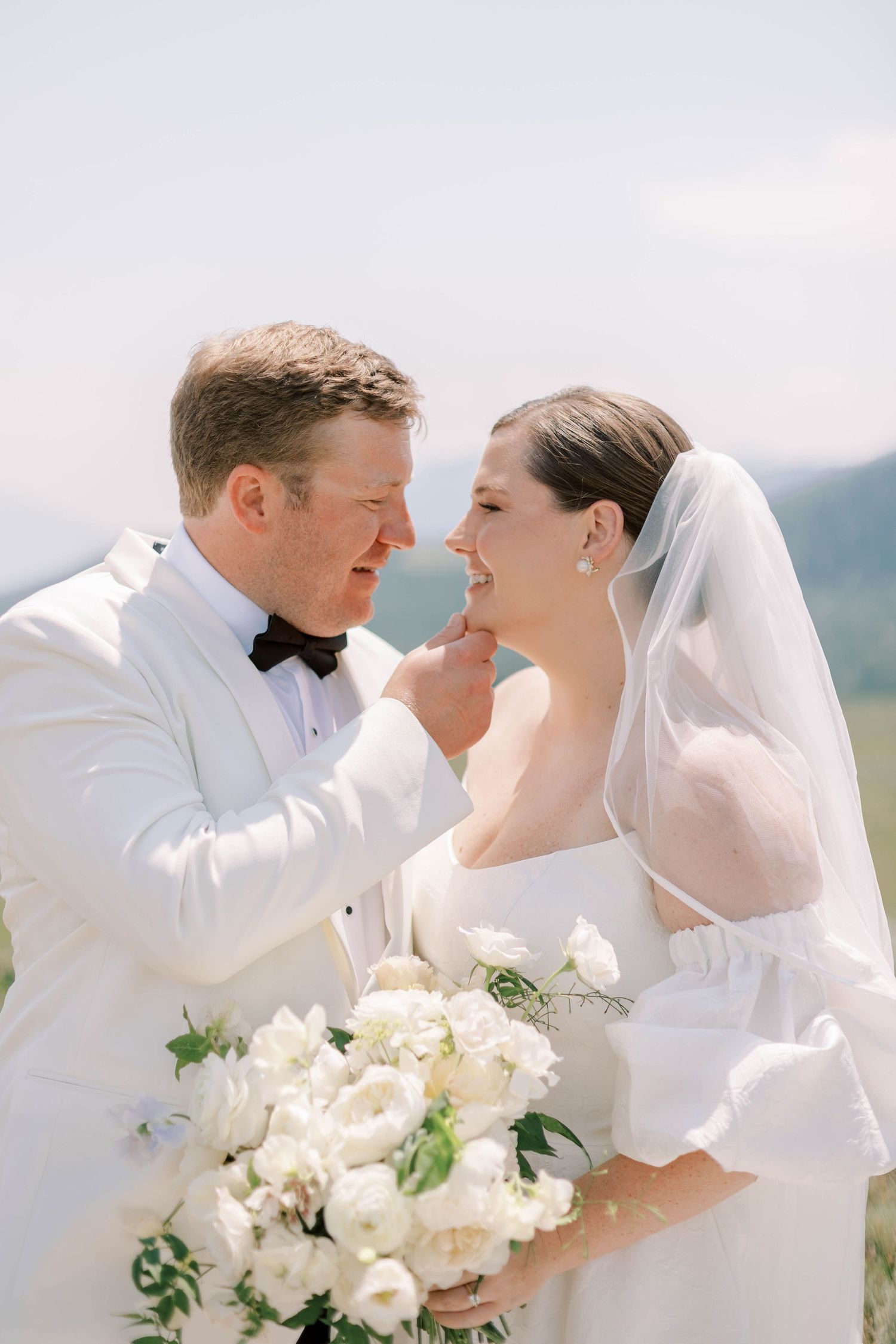 Intimate moment between bride and groom with white floral bouquet in mountain setting.