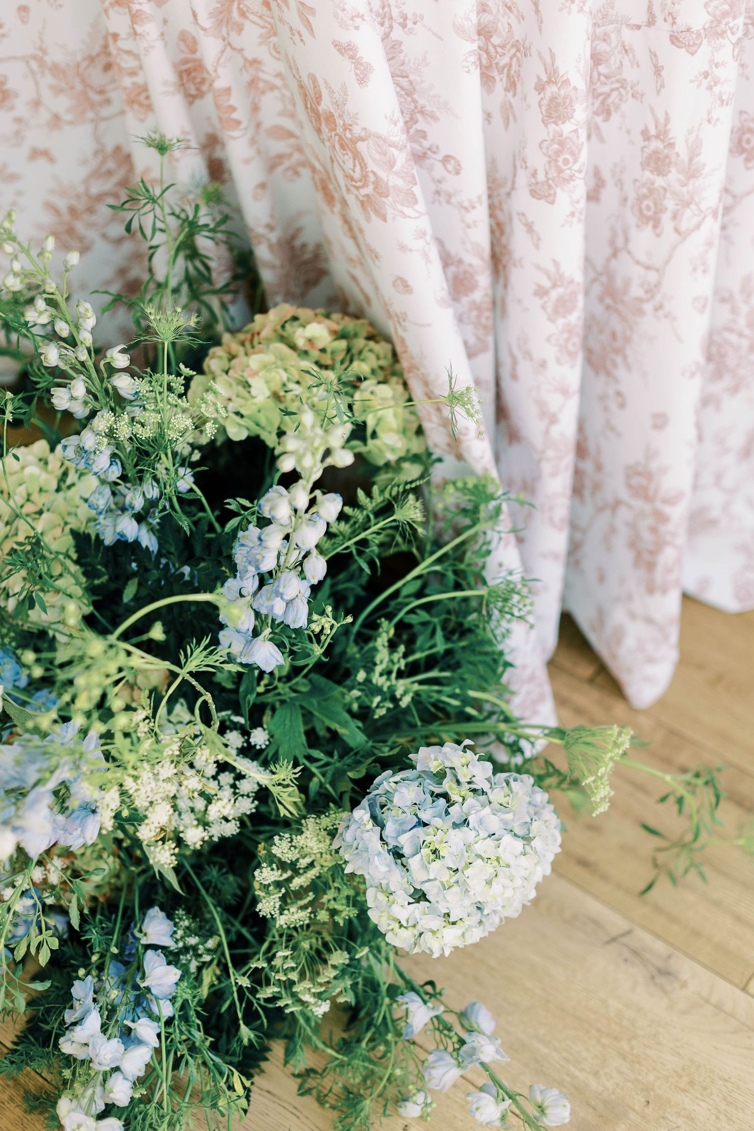 Soft focus close-up of blue and white hydrangea arrangement against floral curtains.
