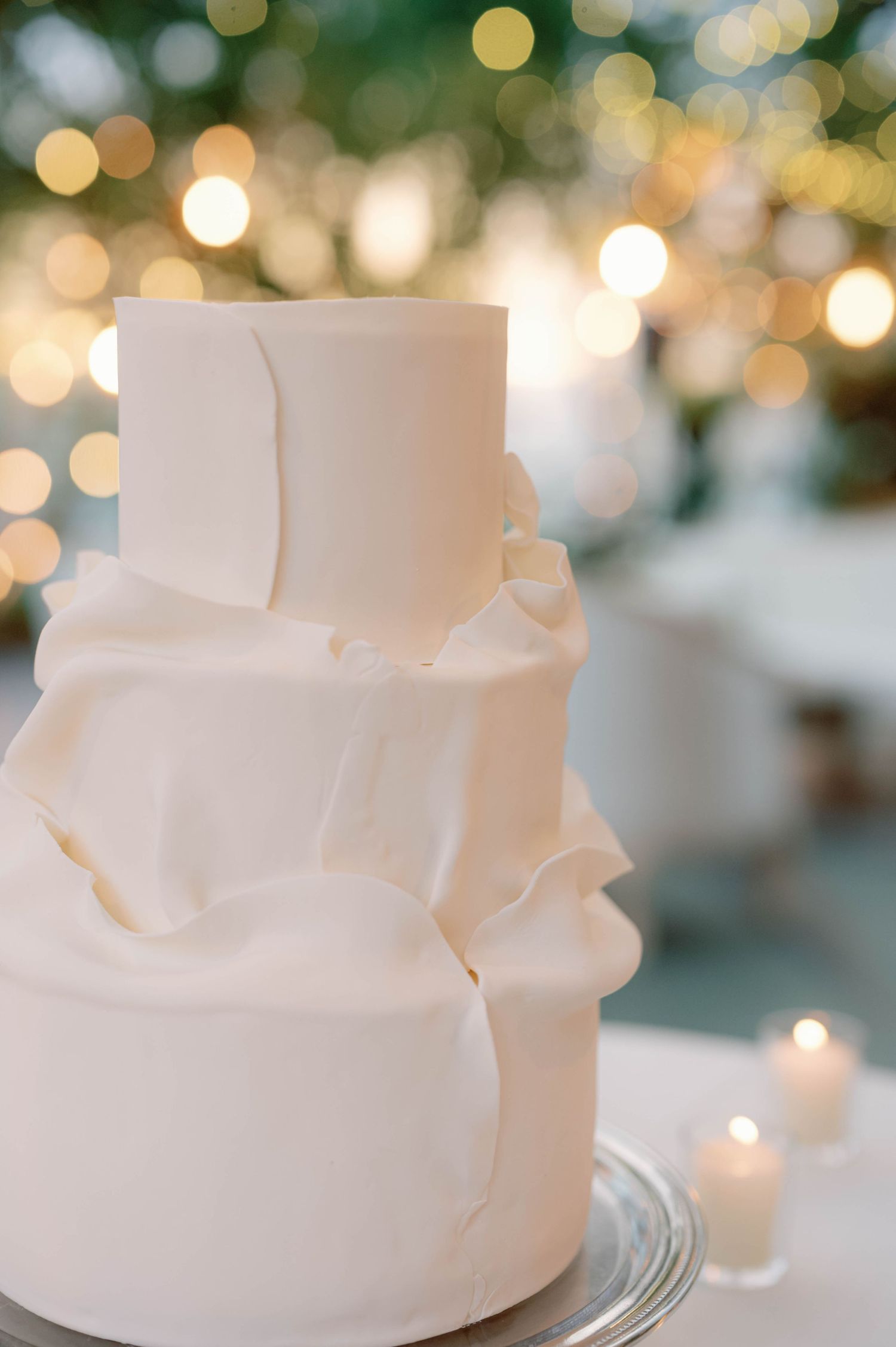 Modern white wedding cake with textured fondant layers against bokeh light background.
