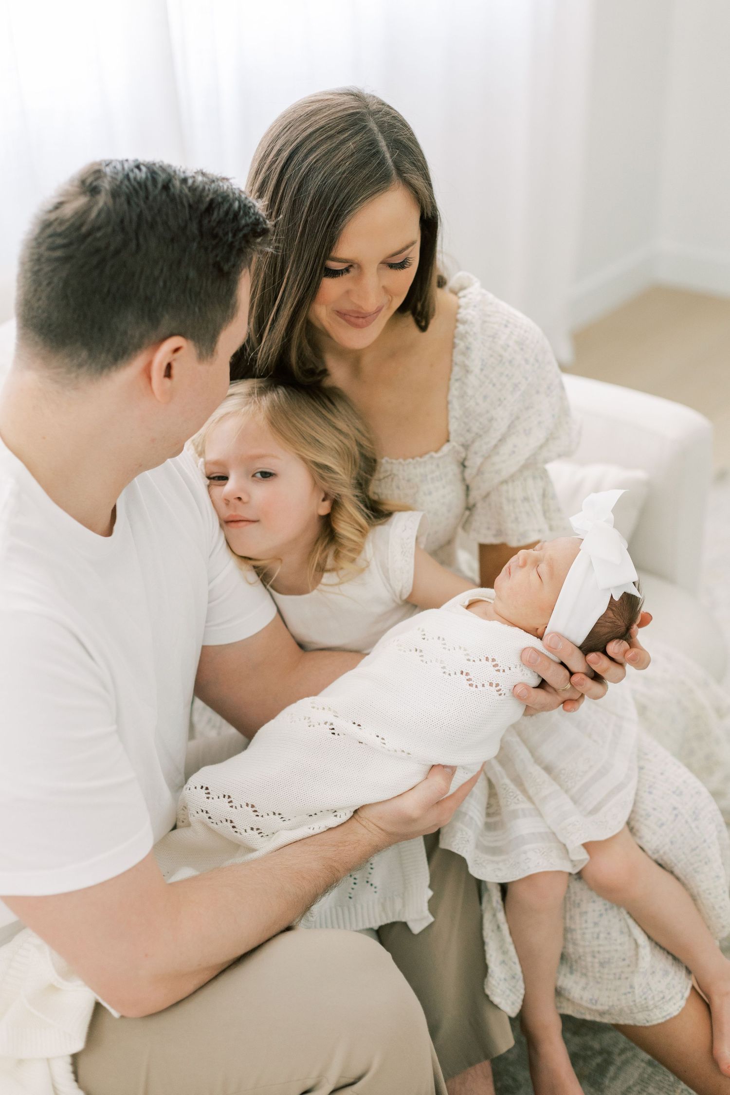 Family sharing an intimate moment together on a couch while holding a newborn baby in white clothing.