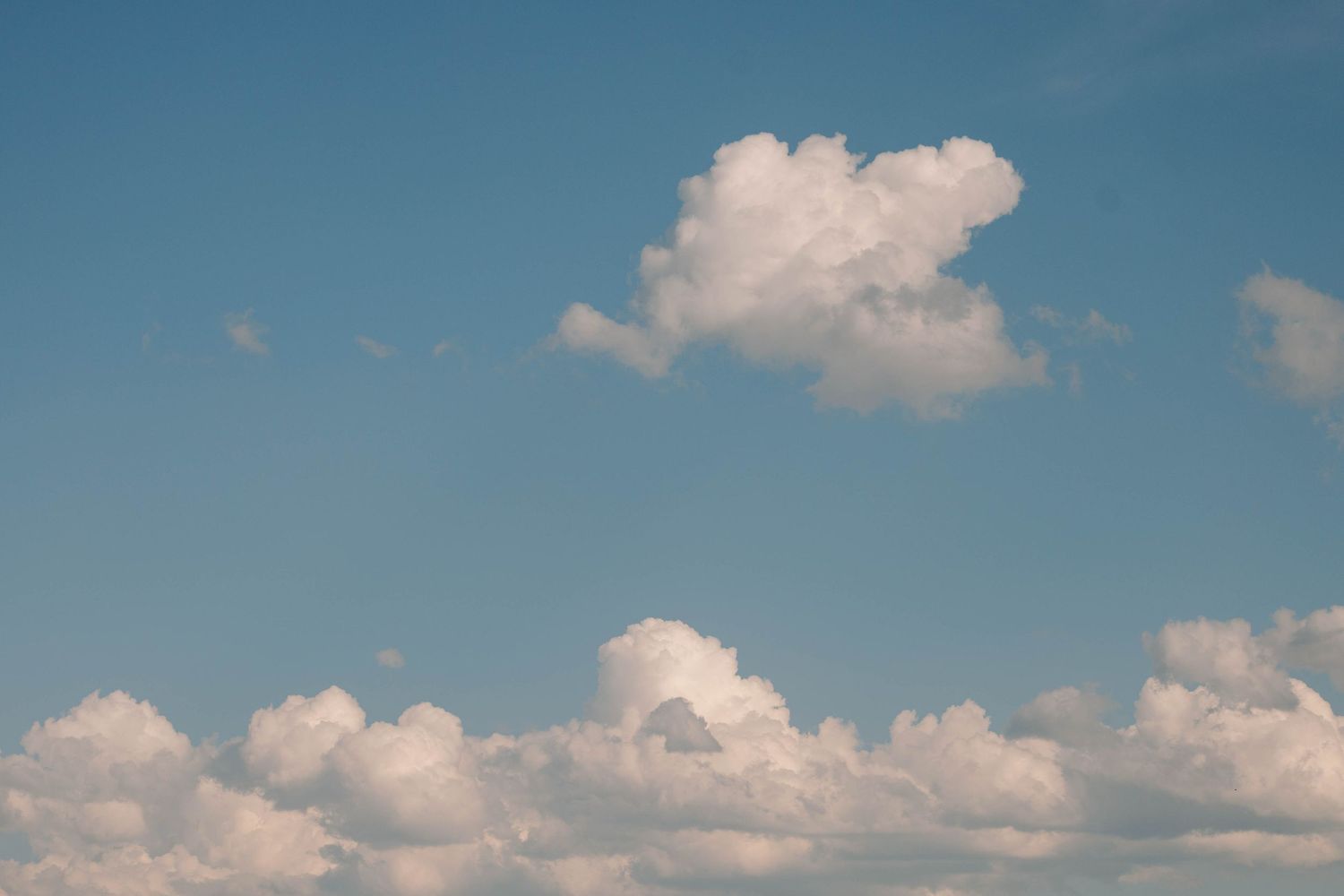 Fluffy white clouds in bright blue summer sky.