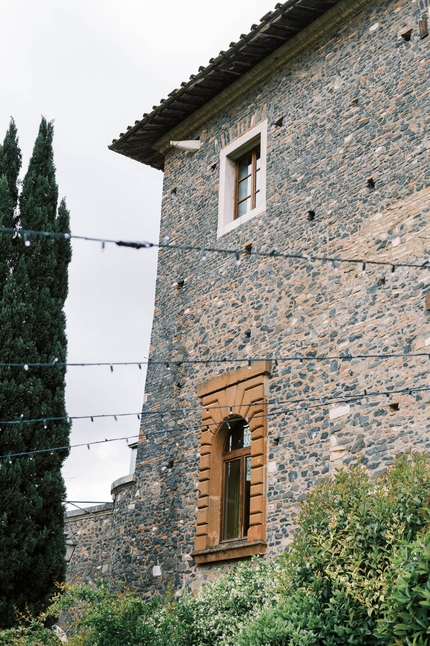 Stone villa with arched window and cypress trees against an overcast sky in Tuscany.