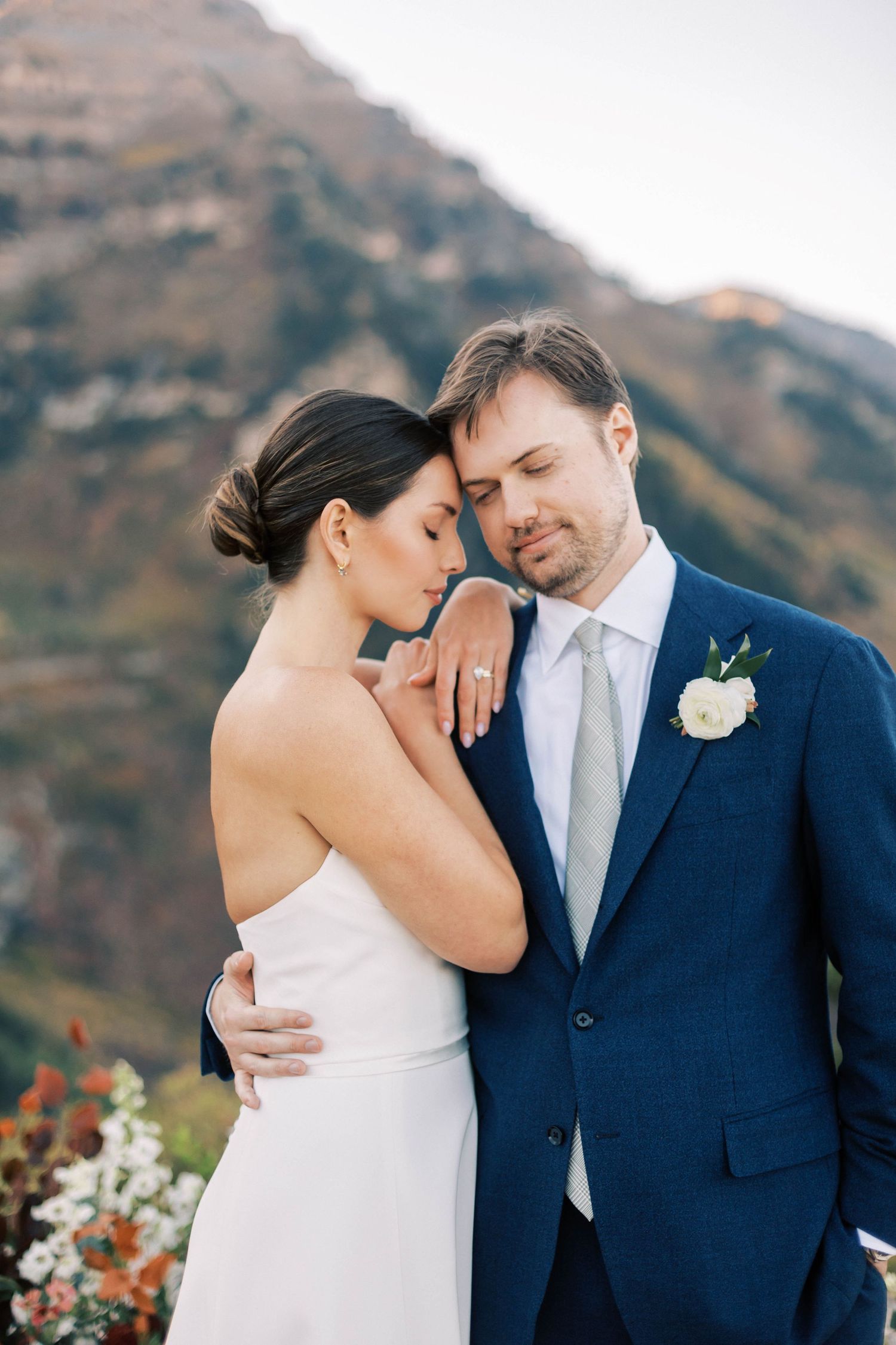 A romantic wedding portrait of a couple embracing outdoors against a mountainous backdrop.