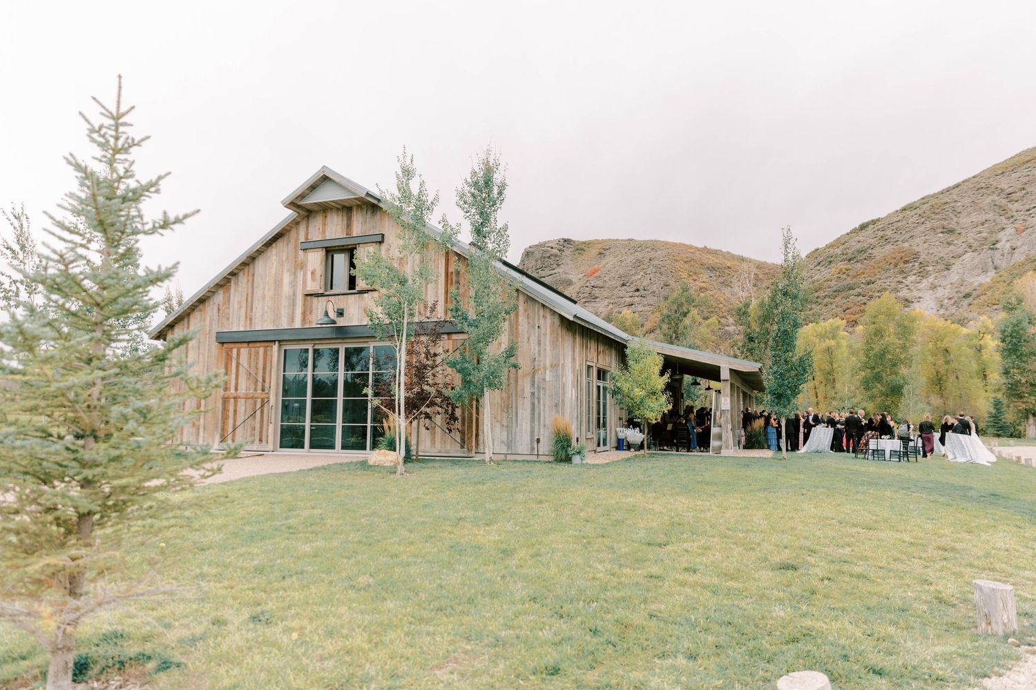 Rustic barn wedding venue with mountain backdrop and evergreen trees.