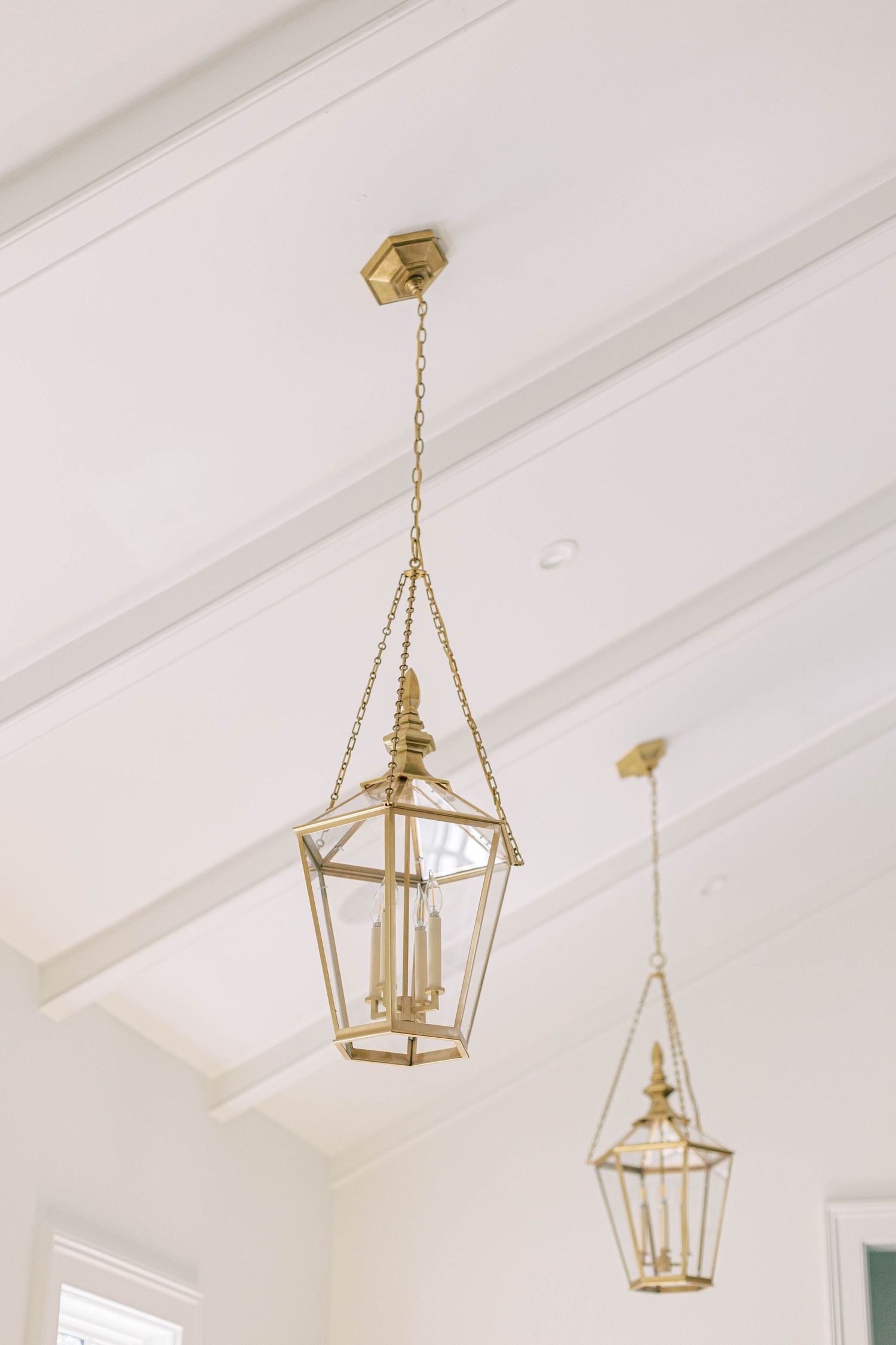 Brass geometric lantern pendant lights hang from a white vaulted ceiling.