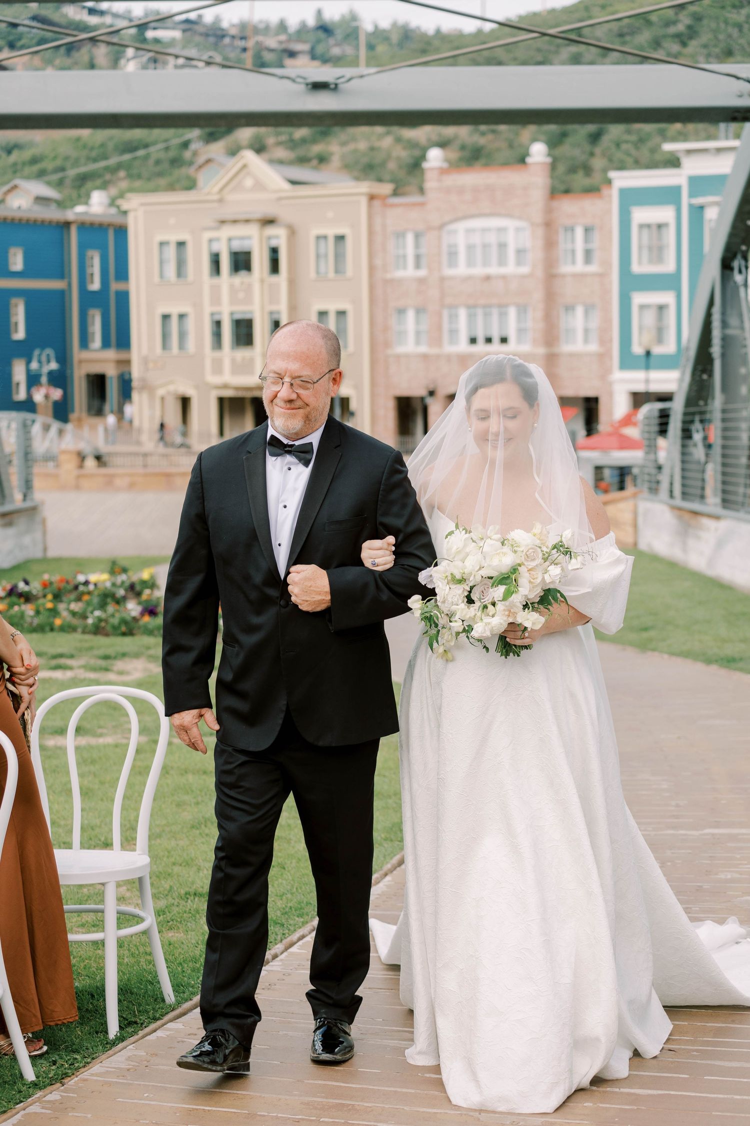 Wedding ceremony processional on a mountain venue deck with colorful buildings in background.