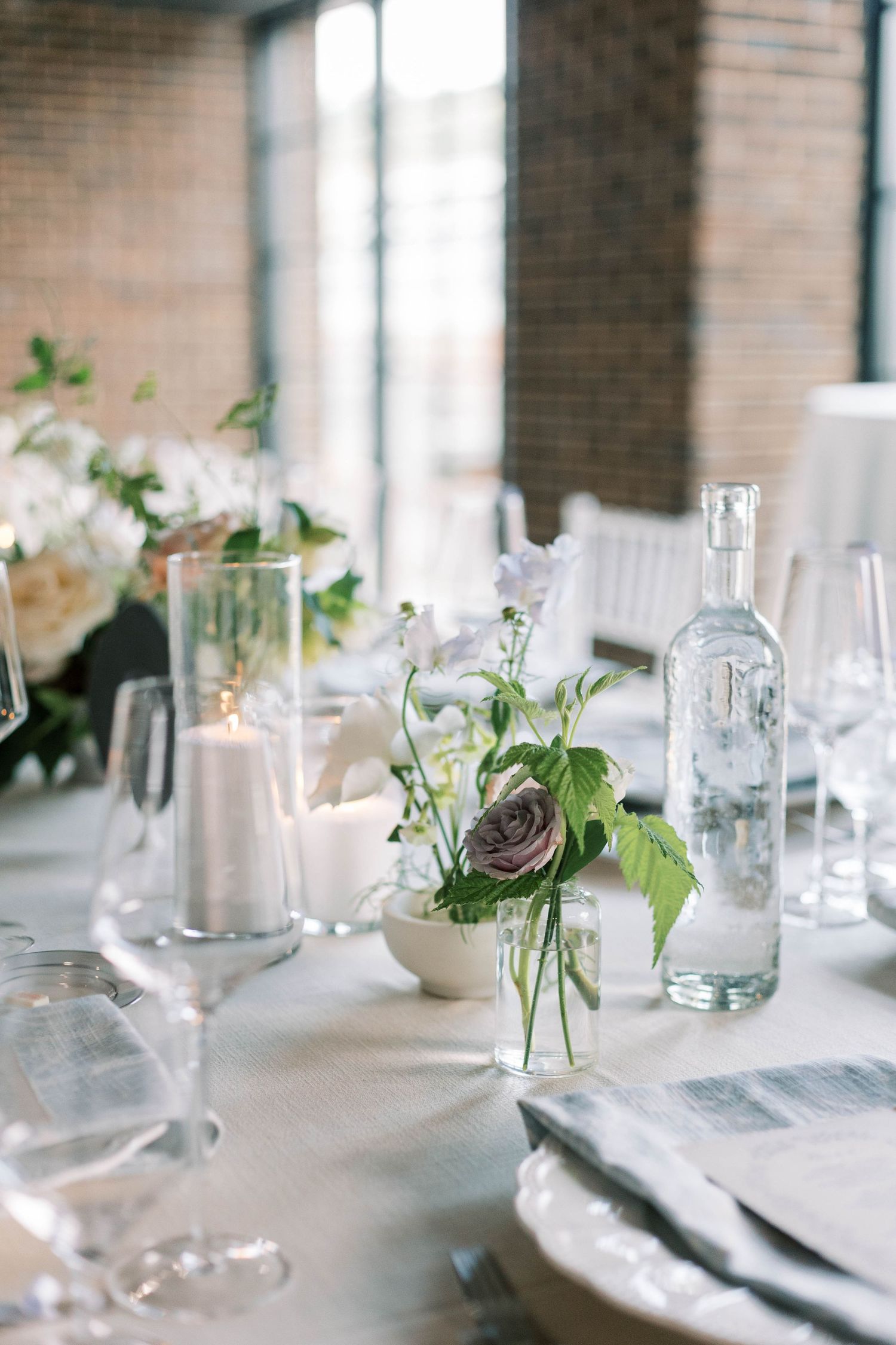 Minimalist wedding table decor with glass bottles, white flowers and crystal stemware.