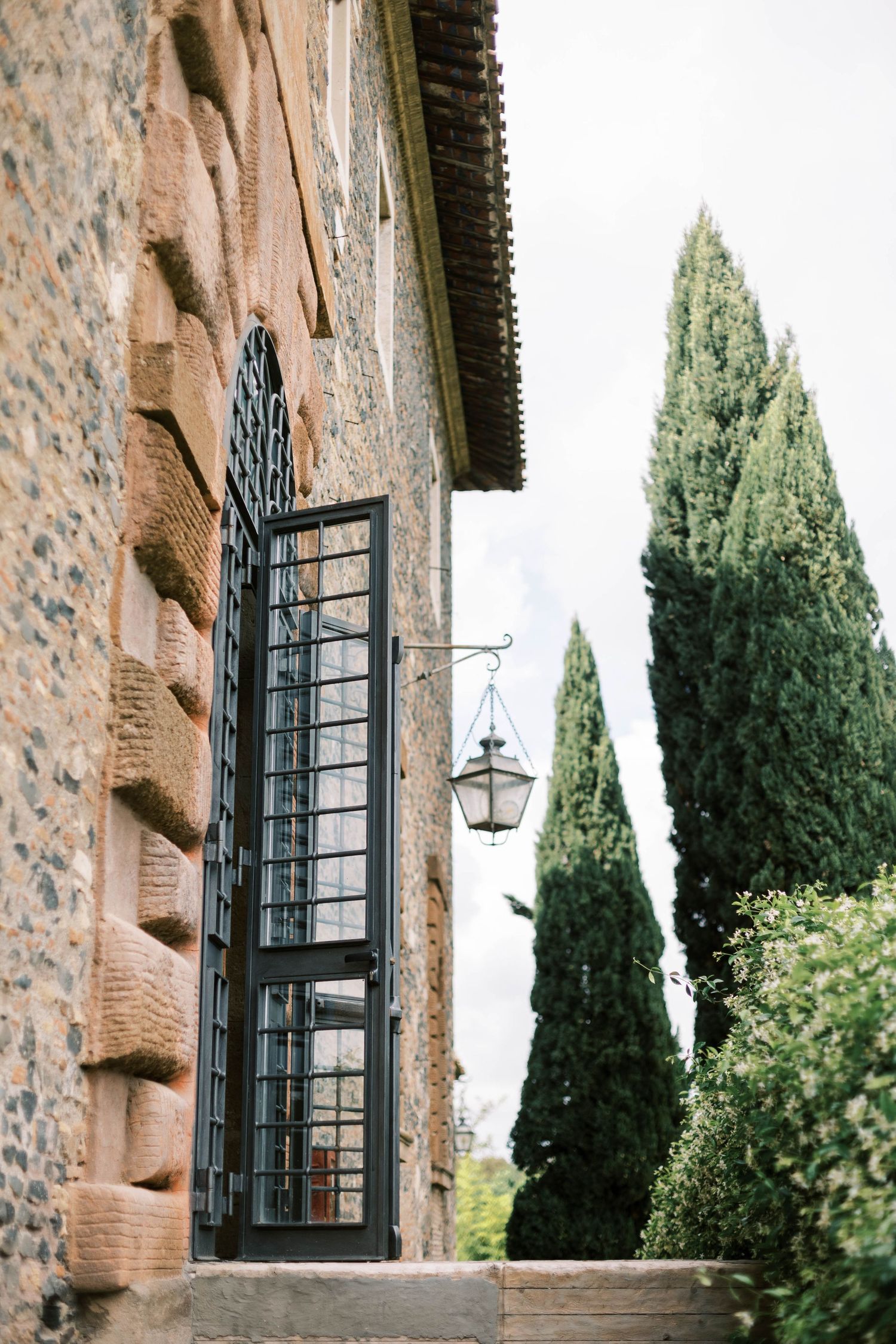 Stone wall exterior of Italian villa with wrought iron details and cypress trees.