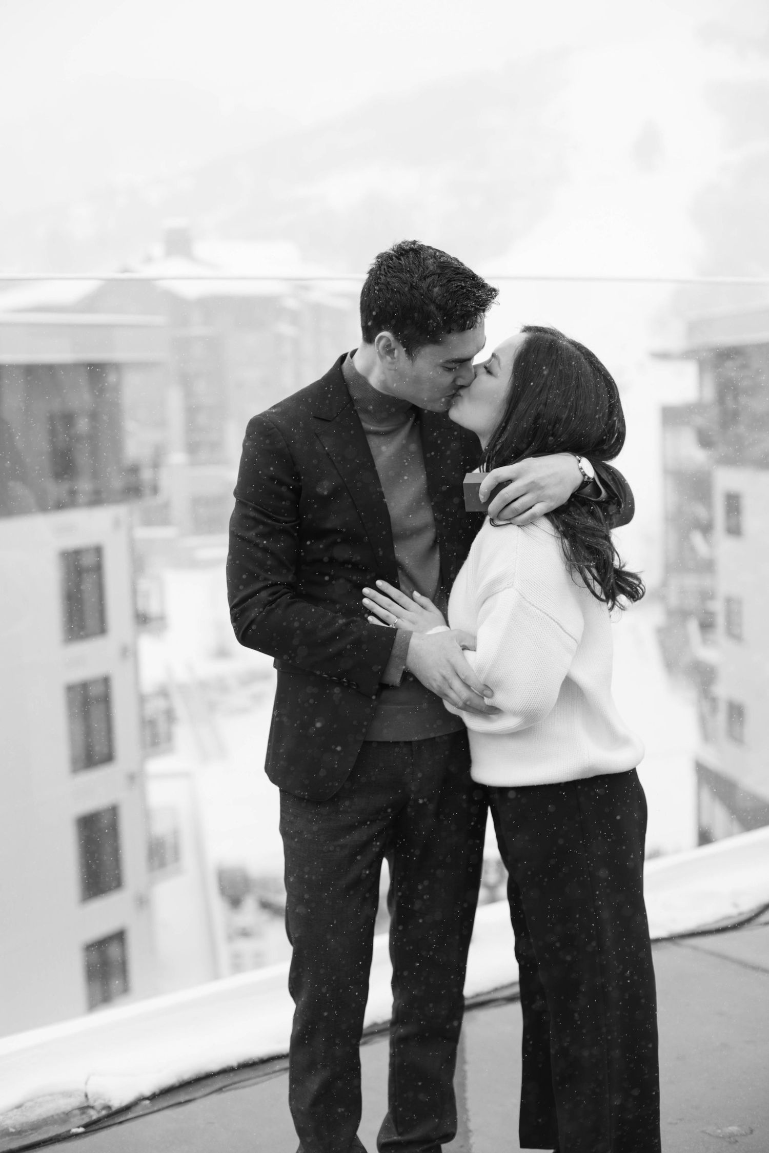 A tender embrace shared on a snow-covered balcony with mountain views in the background at the pendry park city.