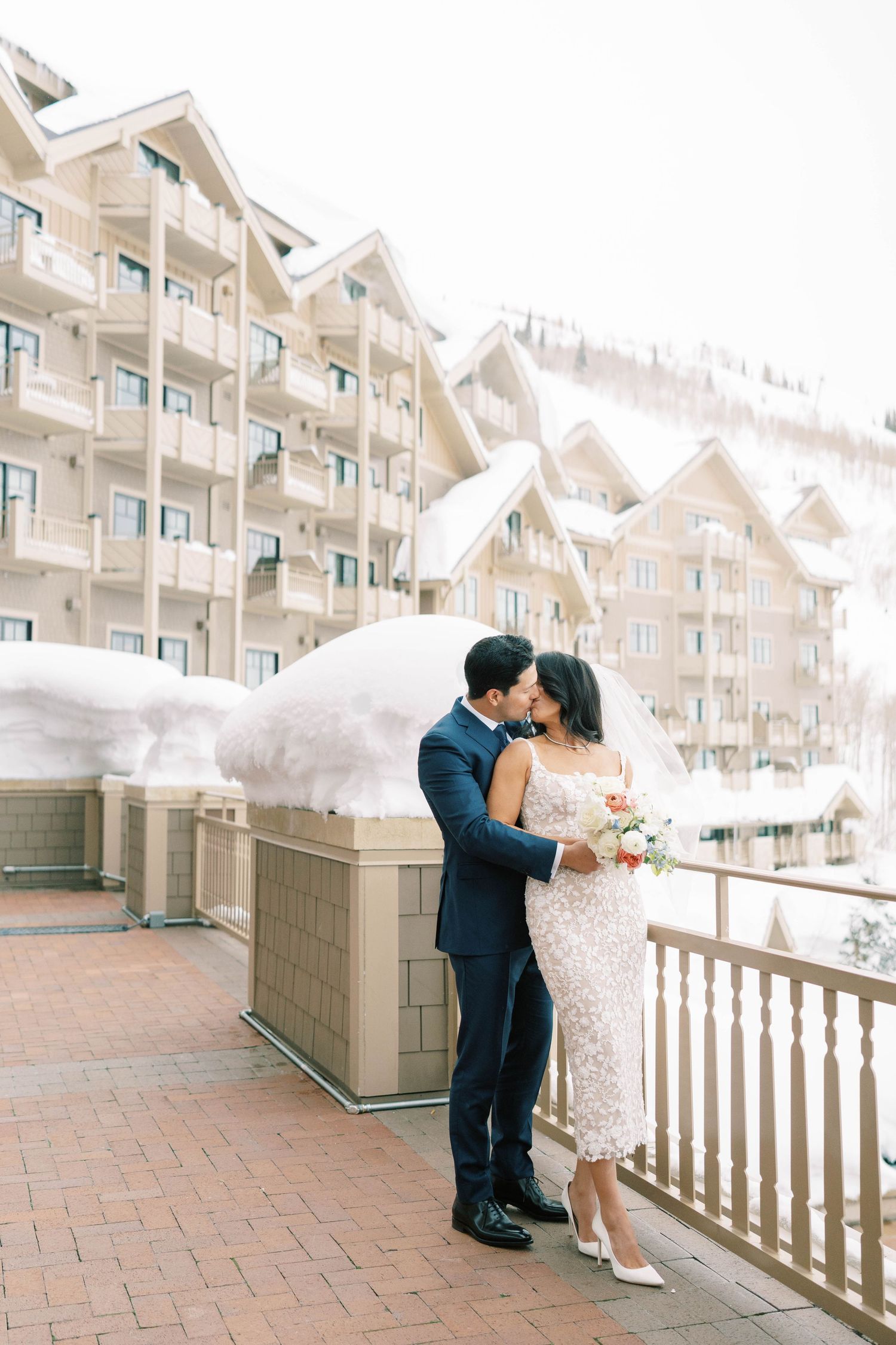 A winter wedding scene with a couple embracing on a terrace overlooking snow-covered mountain architecture at the montage deer valley.
