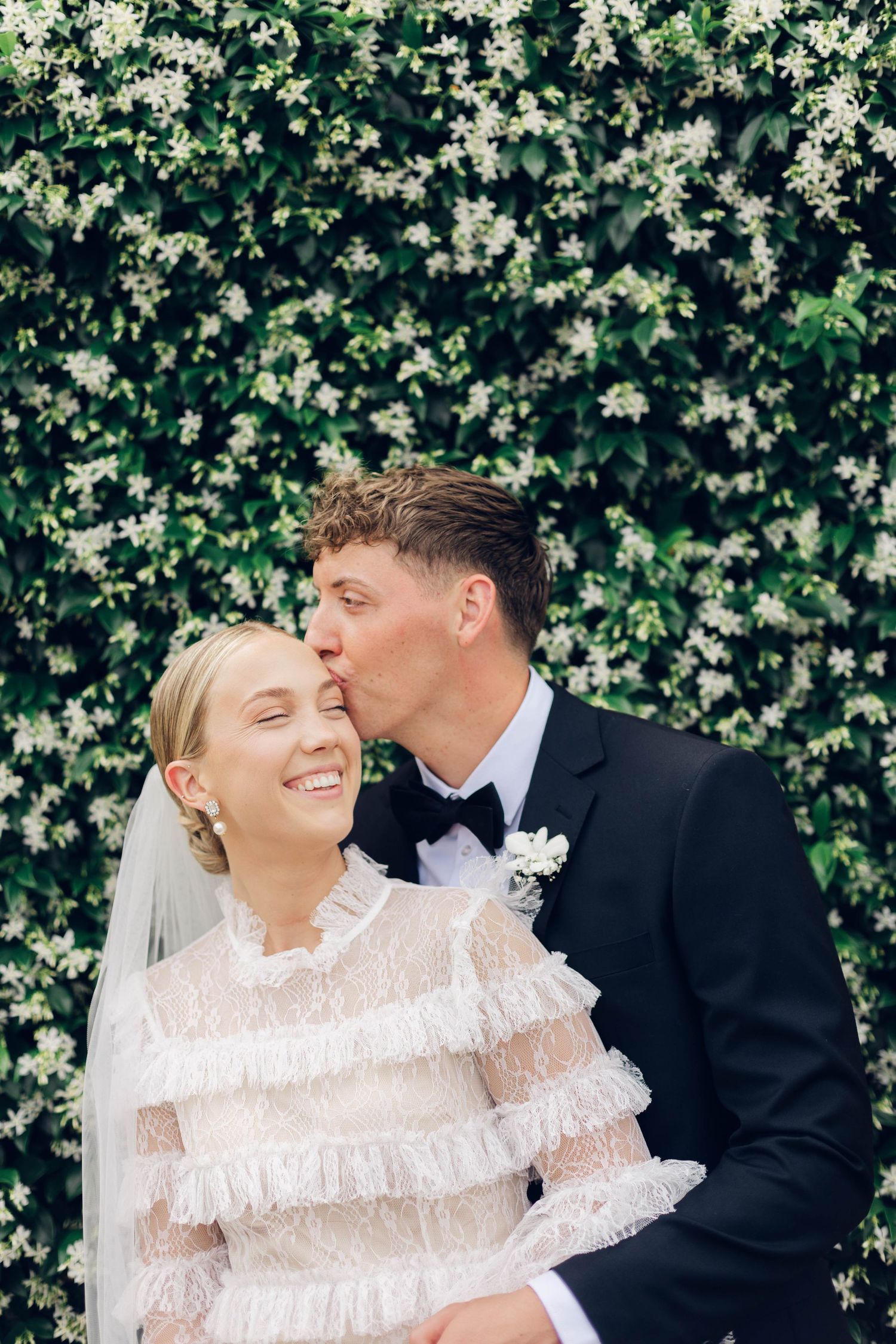 A romantic wedding portrait of newlyweds against a blooming floral backdrop.