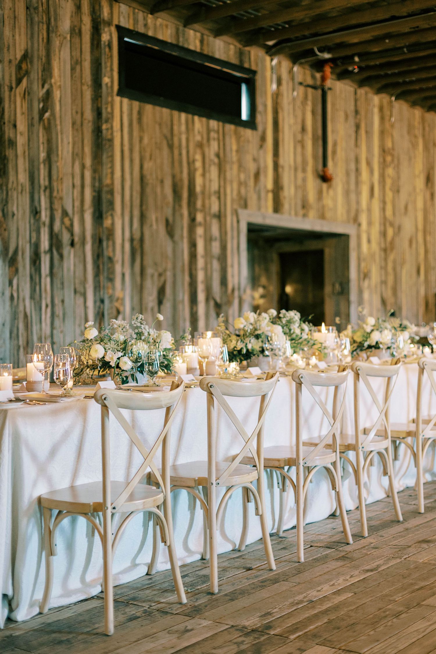 Long banquet table with cross-back chairs and candlelit settings in rustic wooden venue.