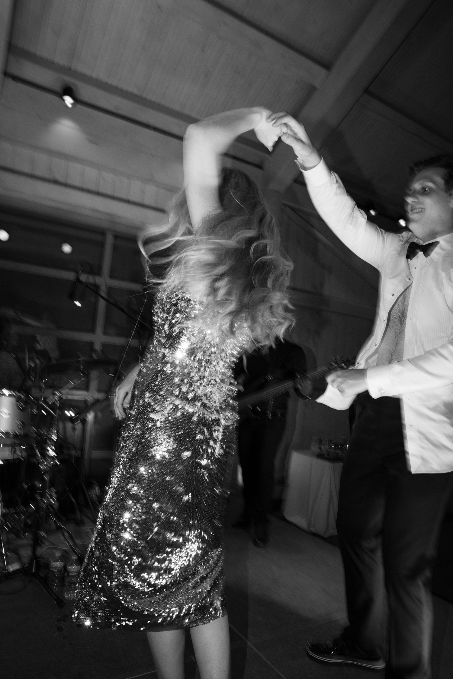 Couple dancing at wedding reception with bride in sparkling sequin dress under venue lighting.