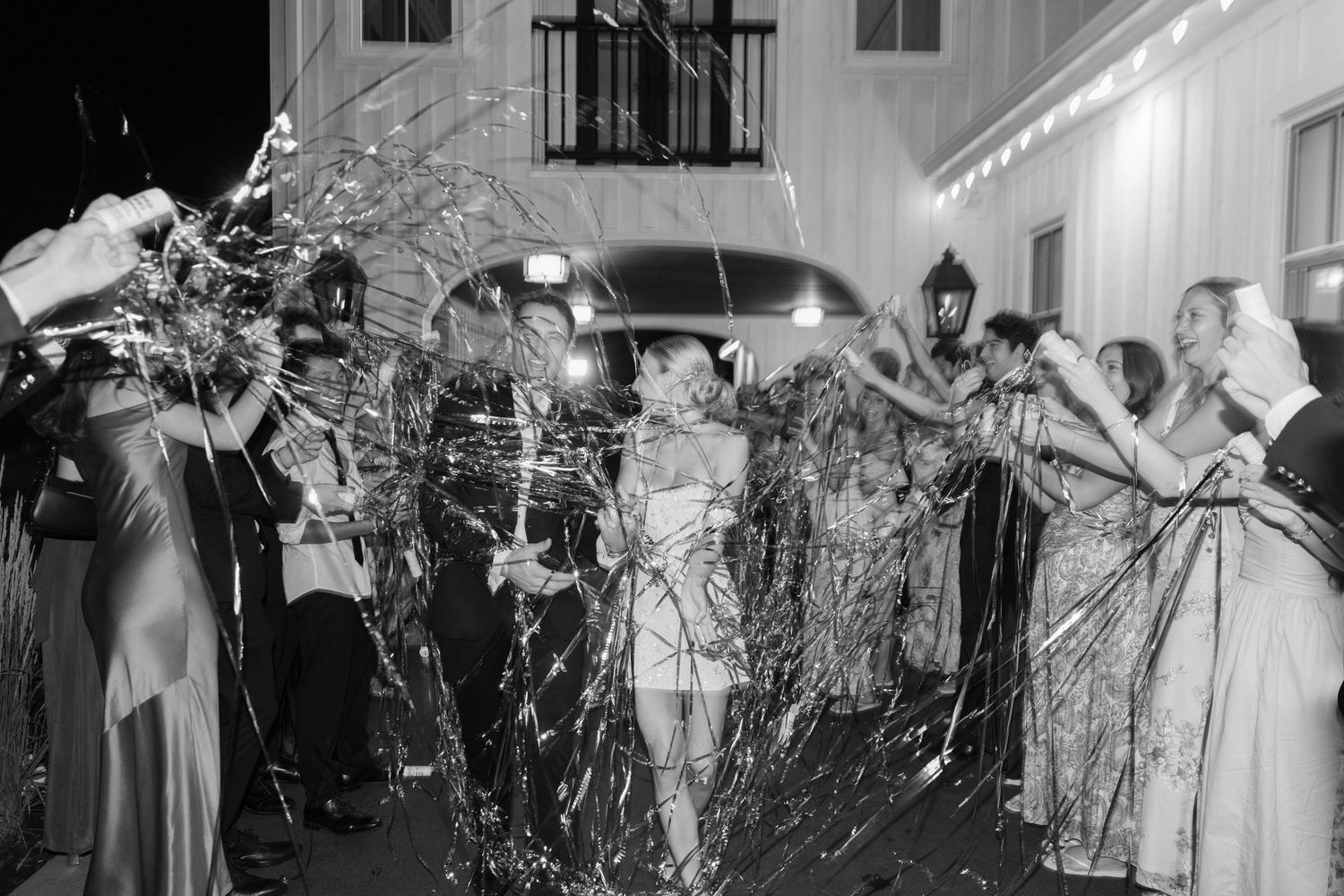 Wedding guests throwing celebratory streamers at night outside a venue.