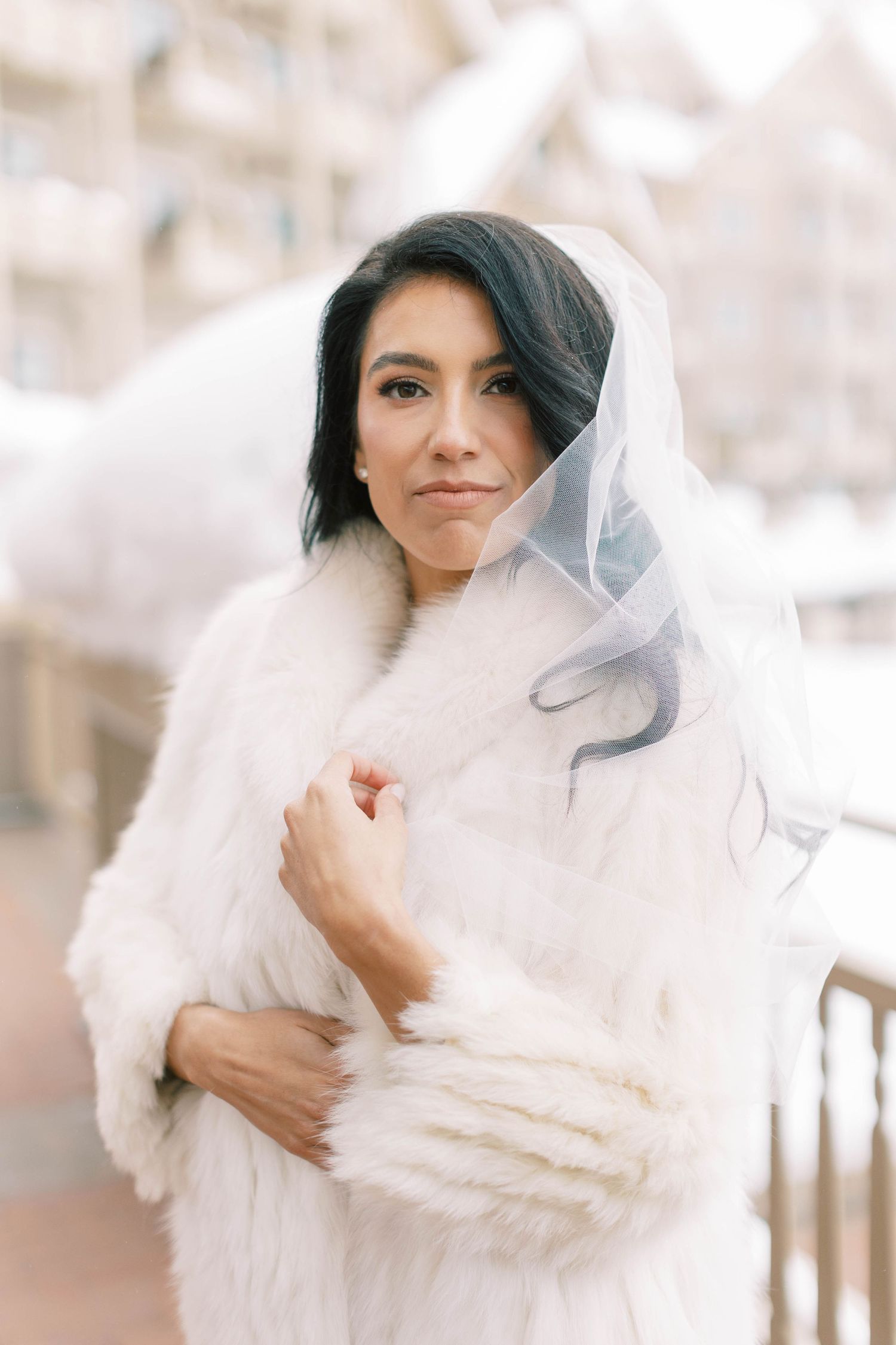 Winter bride wearing a white fur coat and veil against a snowy mountain backdrop at the montage deer valley.