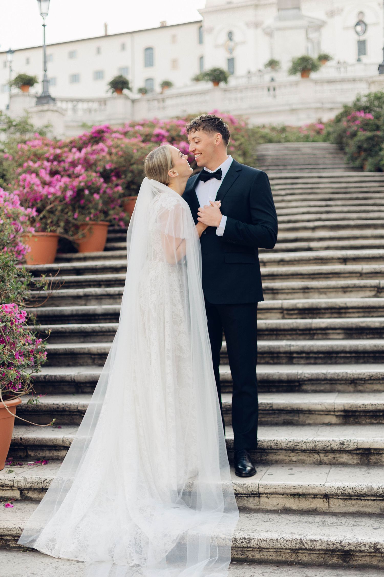 Wedding couple poses on historic stone spanish steps of rome adorned with pink bougainvillea flowers of rome italy