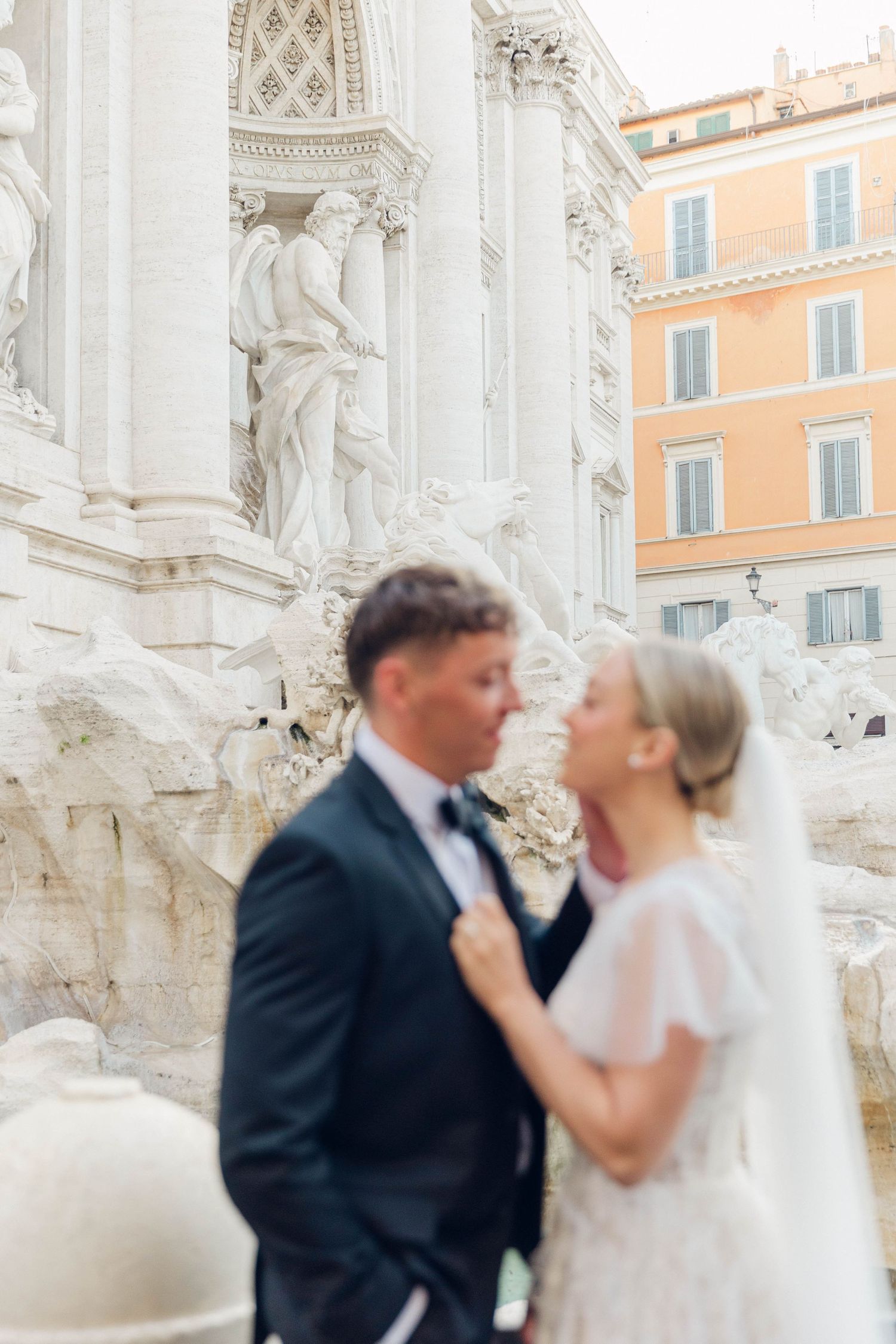 Romantic wedding portrait against the white marble statues and peach-colored buildings of Rome.