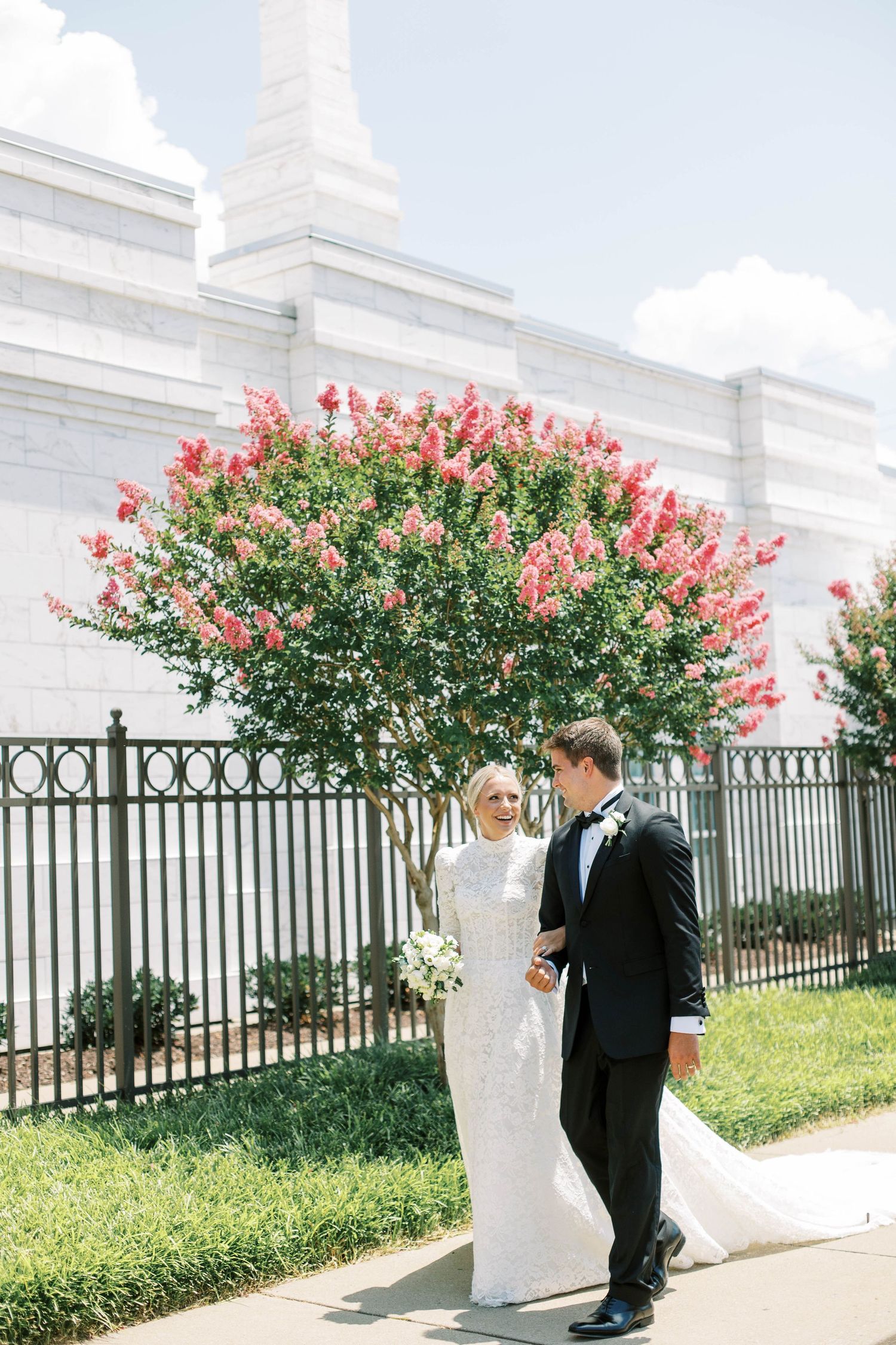 Newlyweds share a moment by blooming crepe myrtle and white temple walls at the Nashville LDS temple.