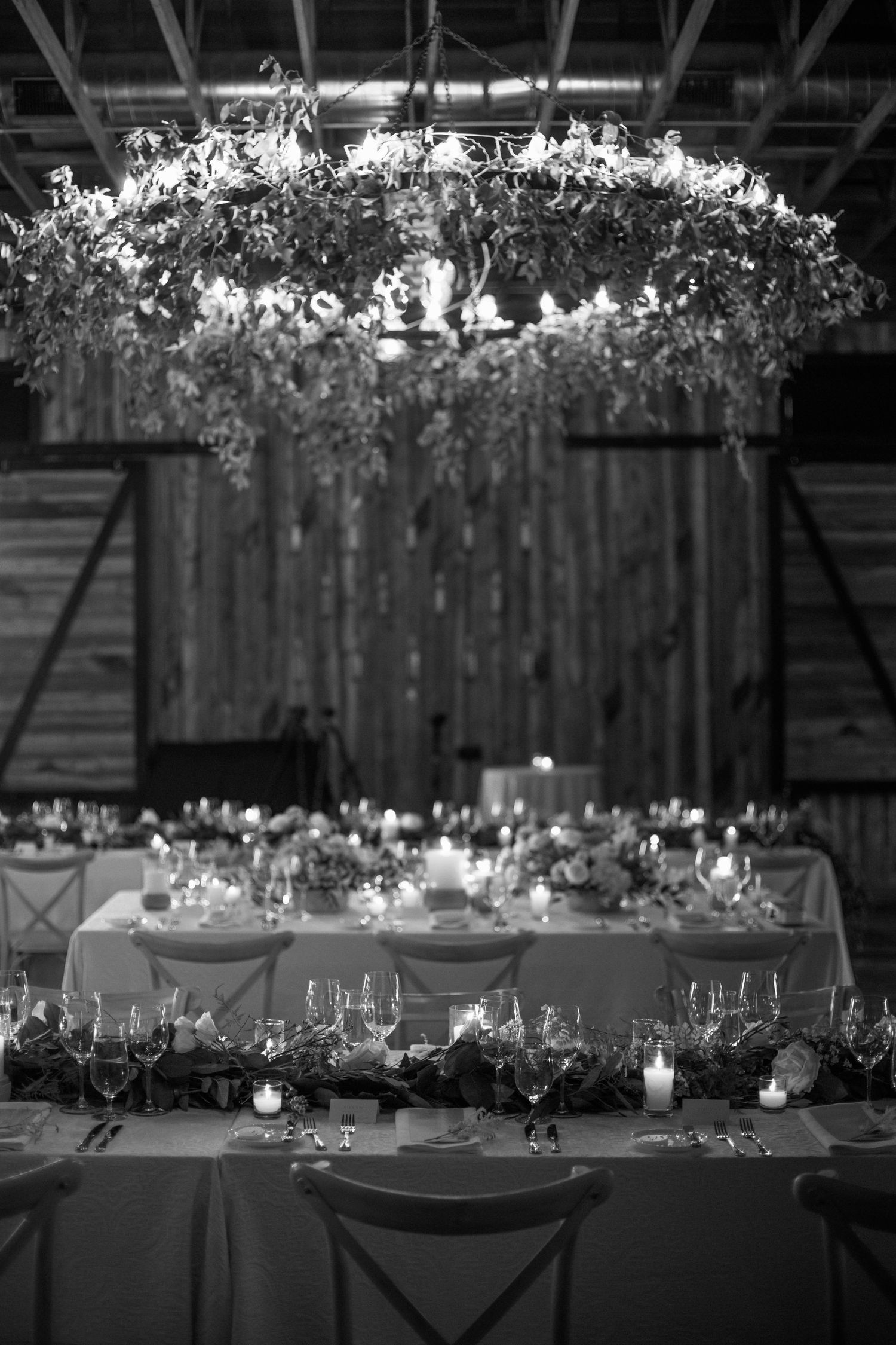Dramatic black and white photo of wedding reception table under circular floral chandelier.