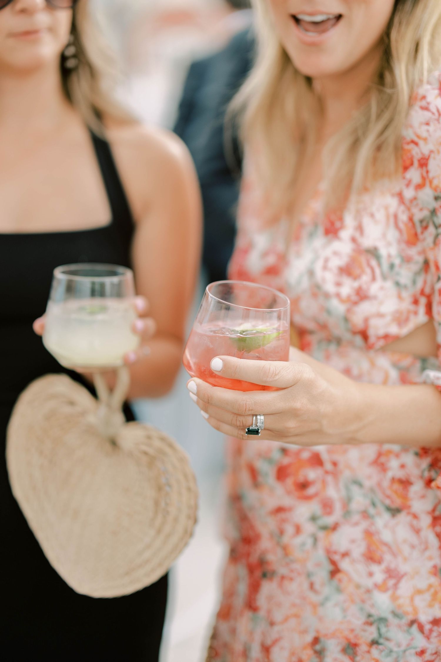 Close-up of cocktail glasses being held at an elegant party with floral dress details.