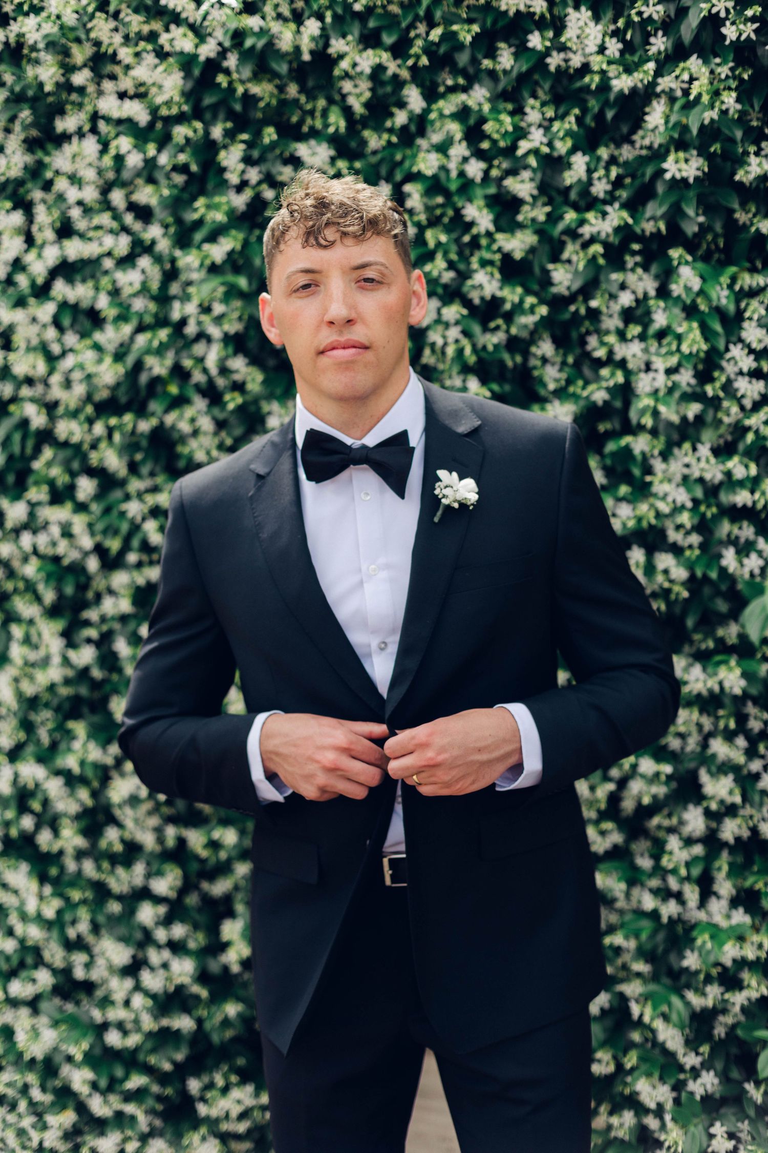 A groom in classic black tuxedo and bow tie poses for a formal portrait.