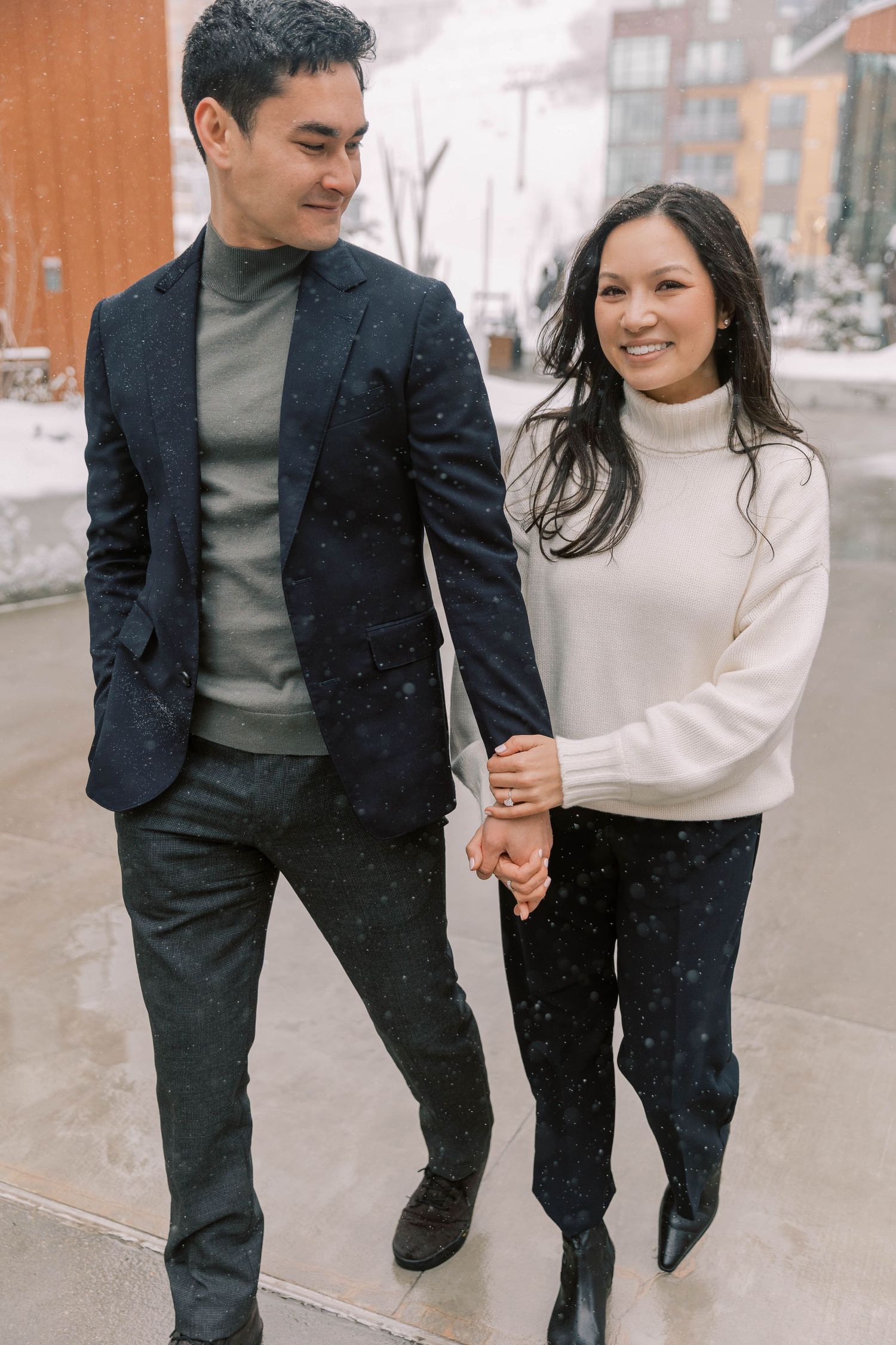 A couple in winter attire holding hands while walking down a snowy urban street.