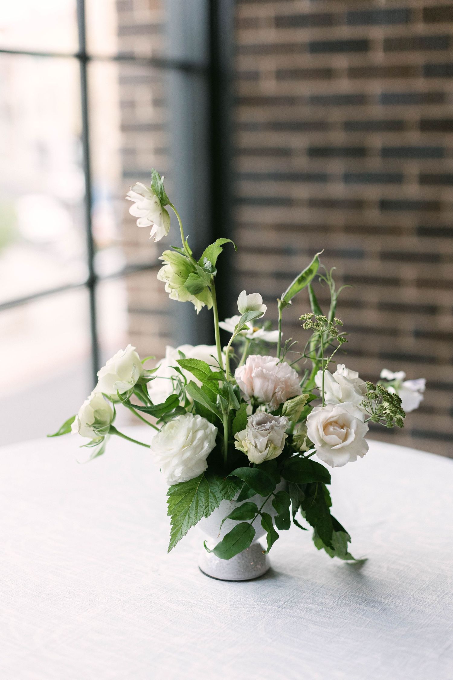 White garden roses and delicate flowers in stone vase against brick window backdrop.