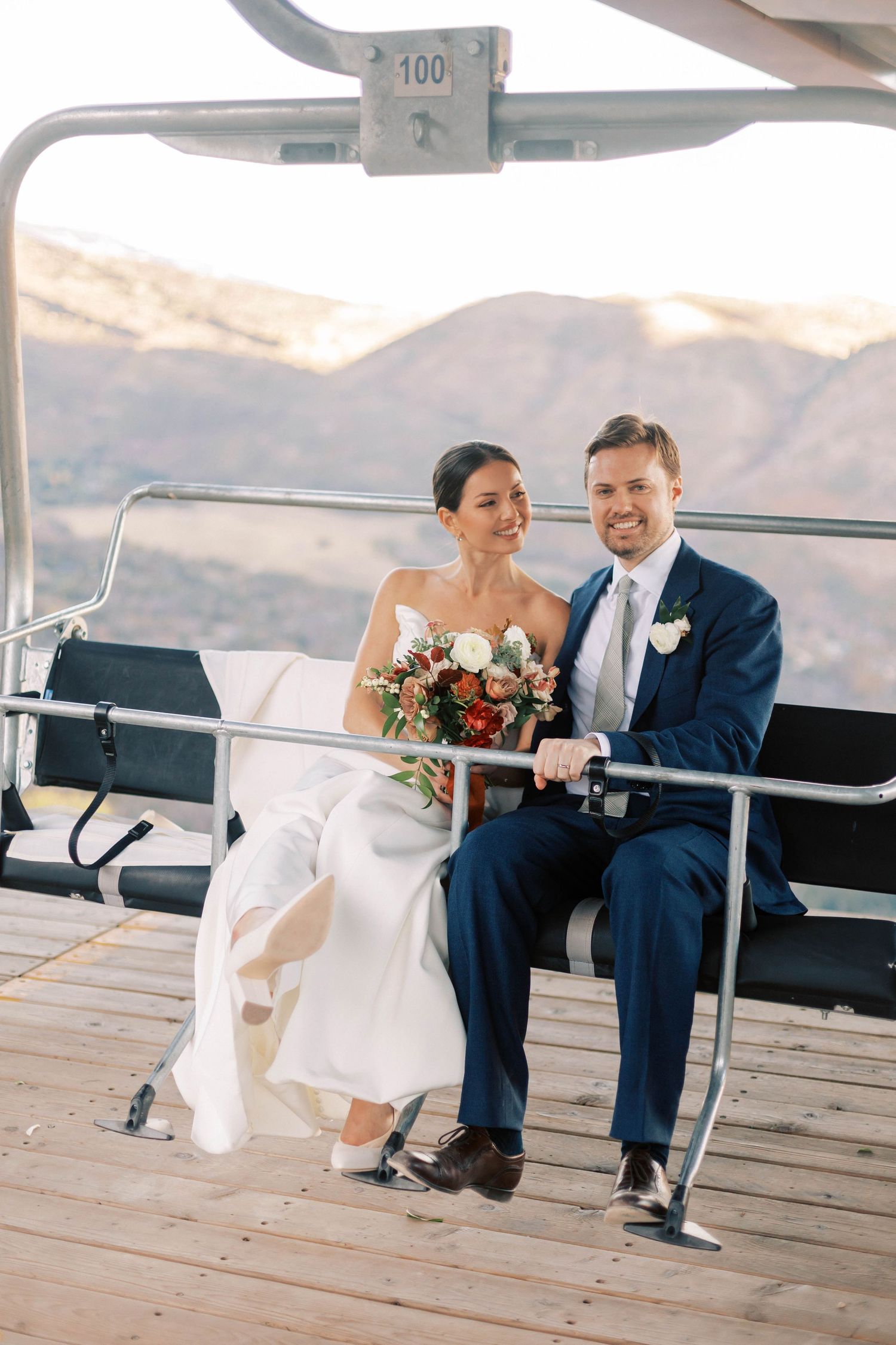 Newlyweds sharing a moment on a ski lift chair with mountain views in the background.