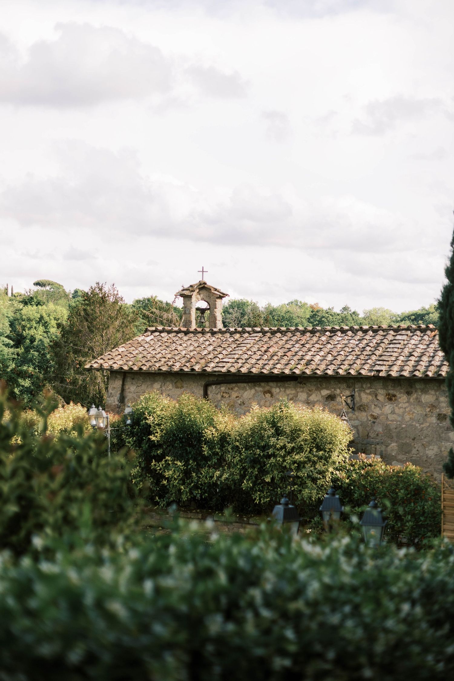 Small stone chapel with terracotta roof tiles nestled among lush green gardens.