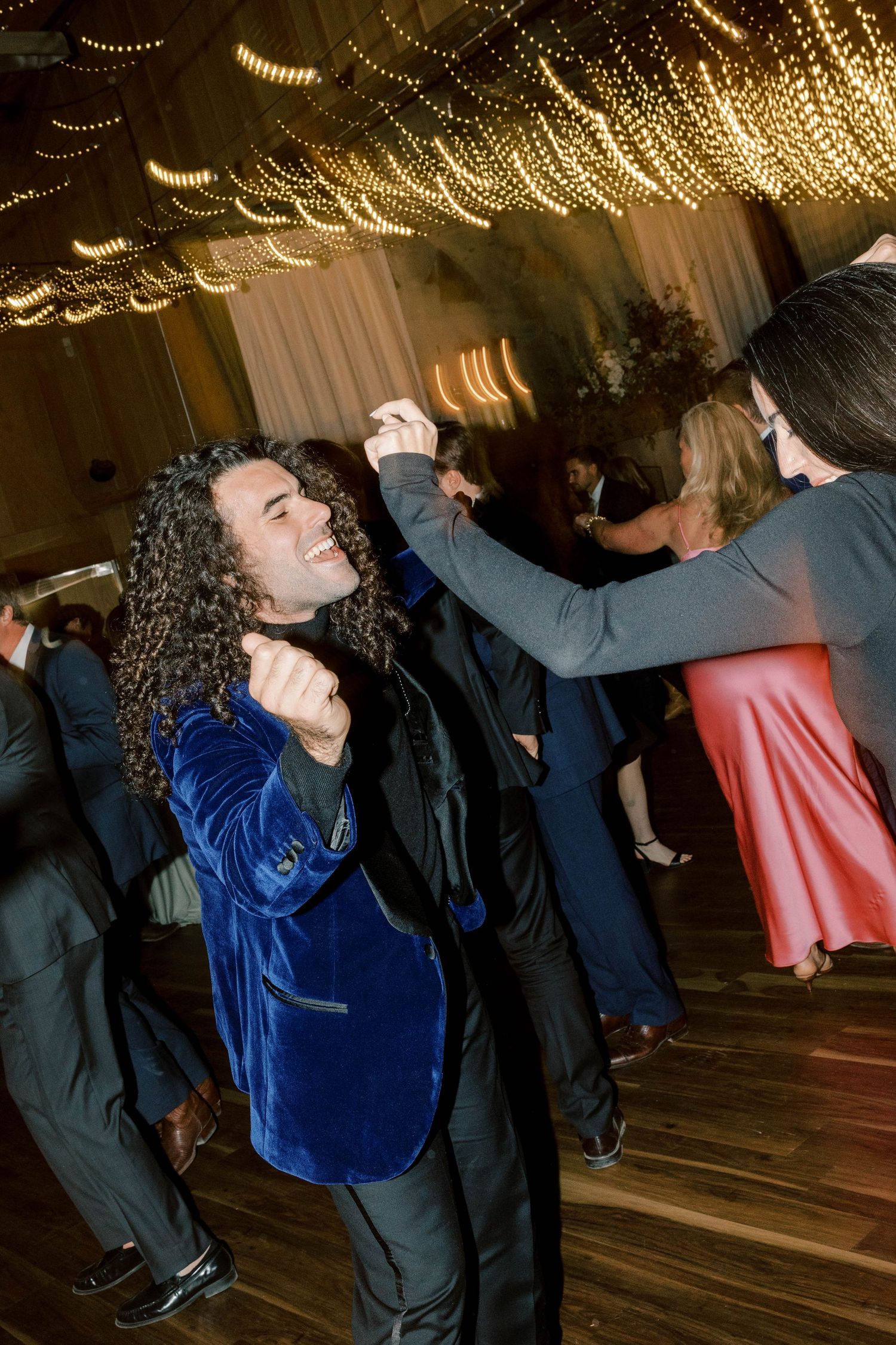 Partygoers dancing under romantic string lights at a wedding reception.