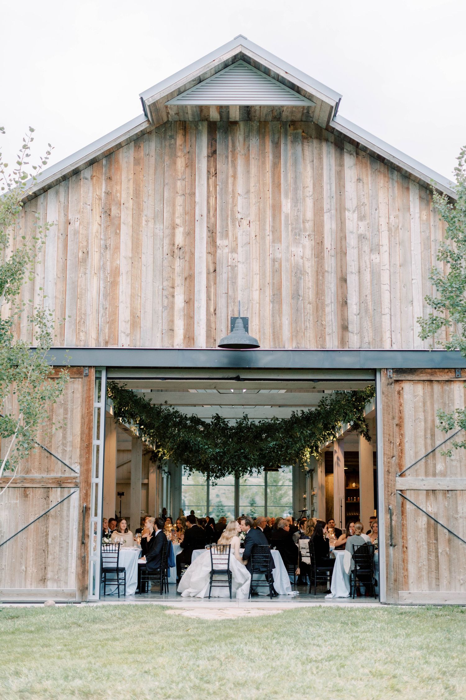 Modern wooden barn venue with large open doors hosting an elegant indoor wedding reception.