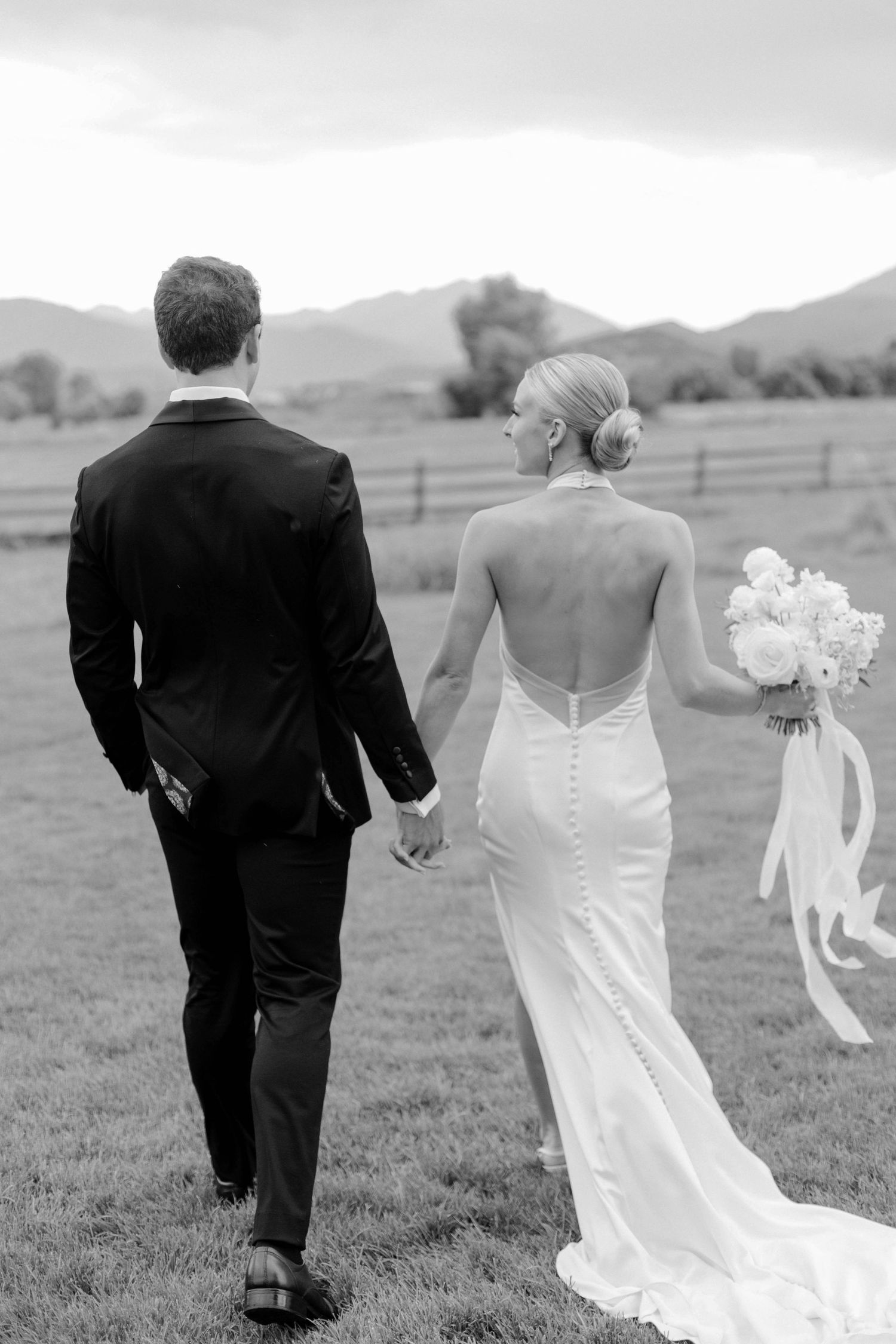 Black and white photo of couple walking through countryside field on their wedding day.