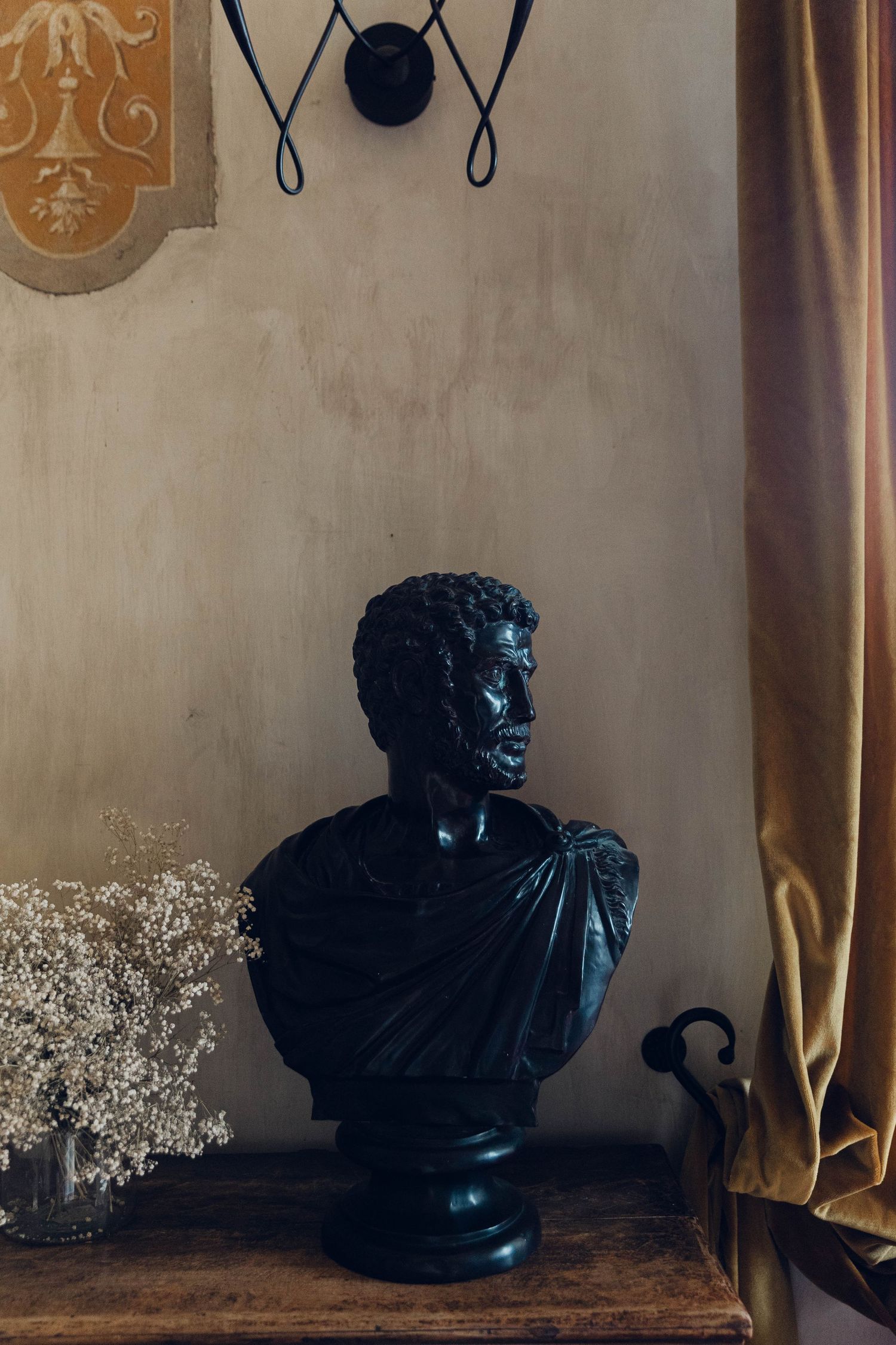 Black classical bust sculpture displayed on wooden table with drapery in background.