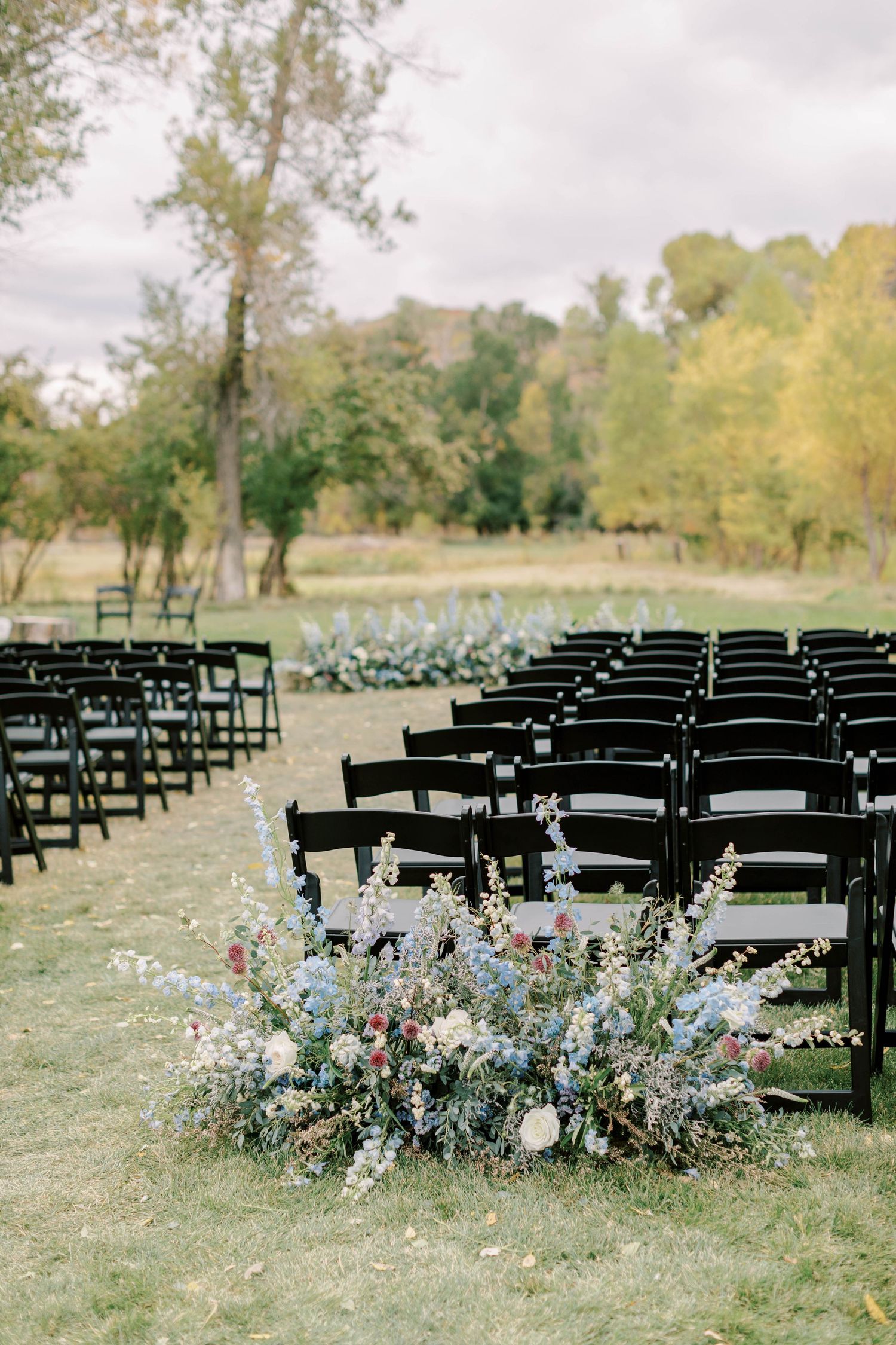 Black chairs arranged for an outdoor ceremony with delicate floral arrangements lining the aisle.