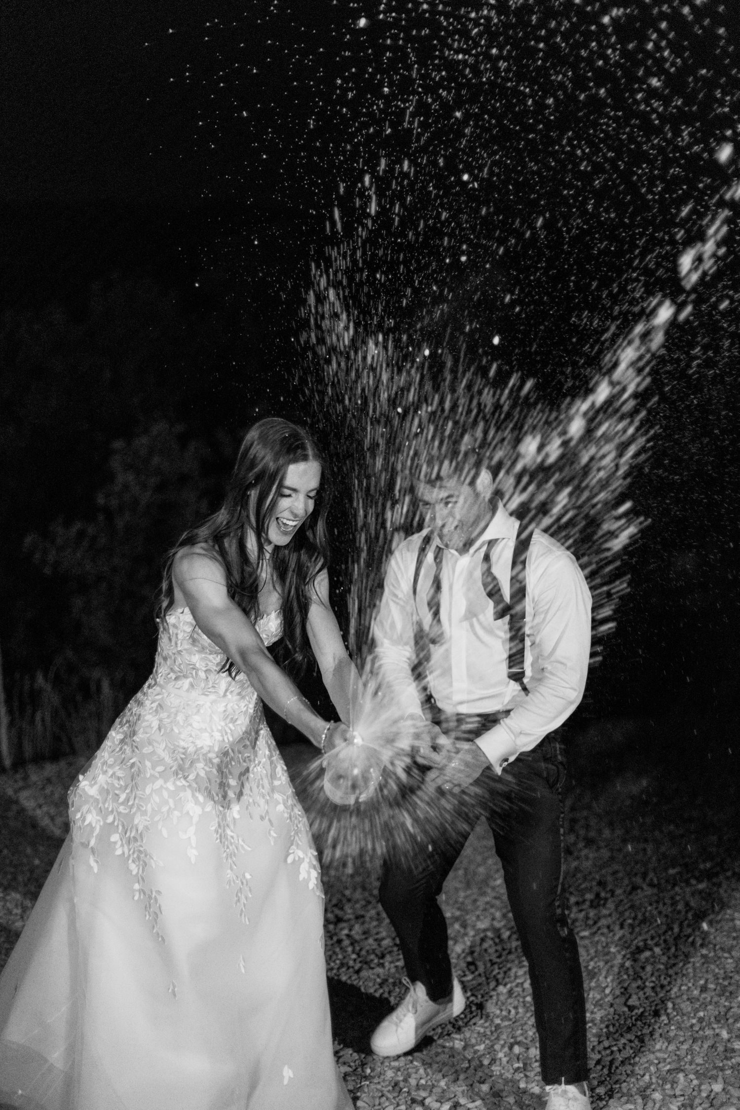 Newlyweds playfully splash champagne during their wedding celebration at night.