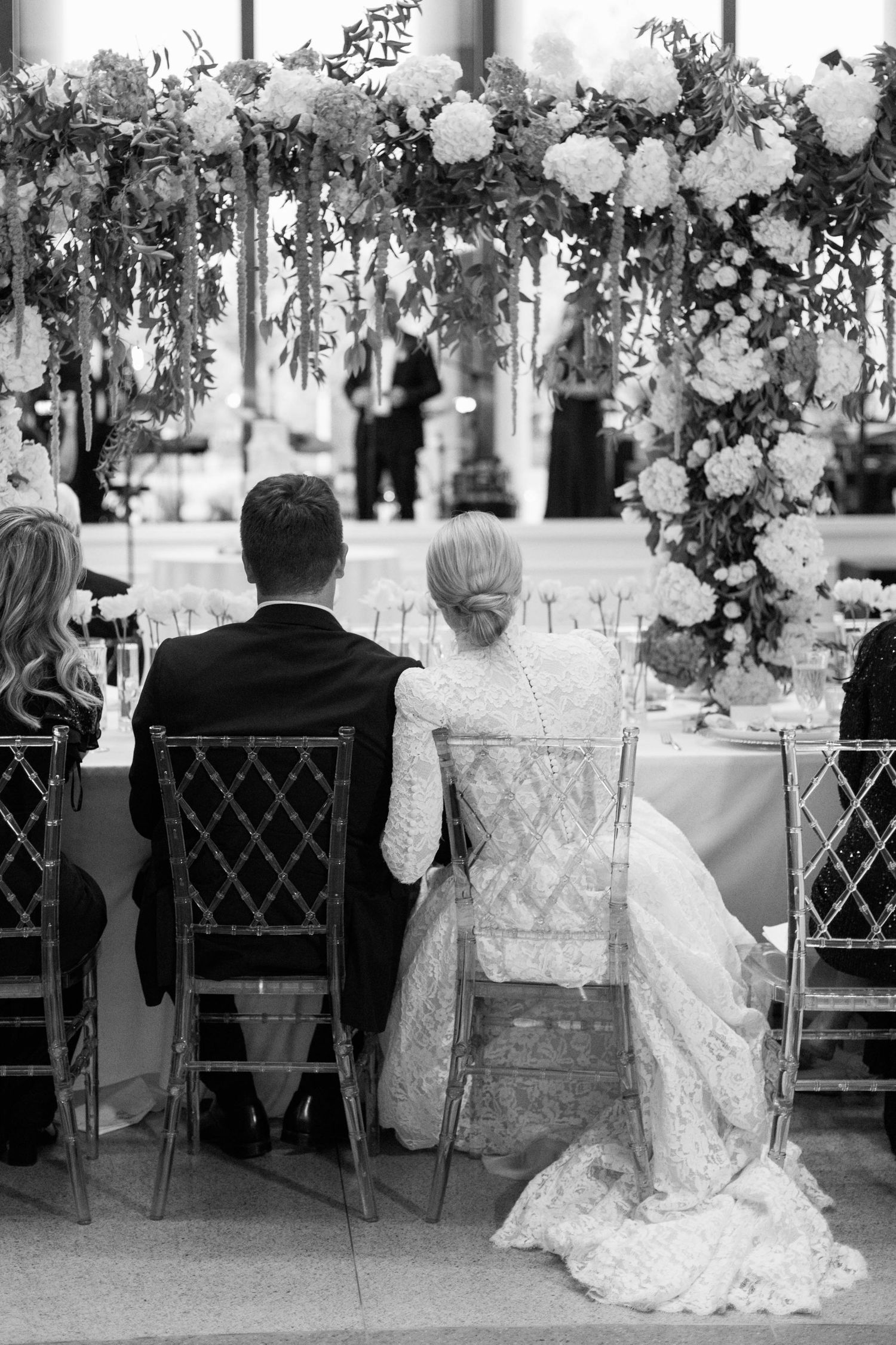 Wedding reception with elaborate floral arch and guests seated at dinner tables.