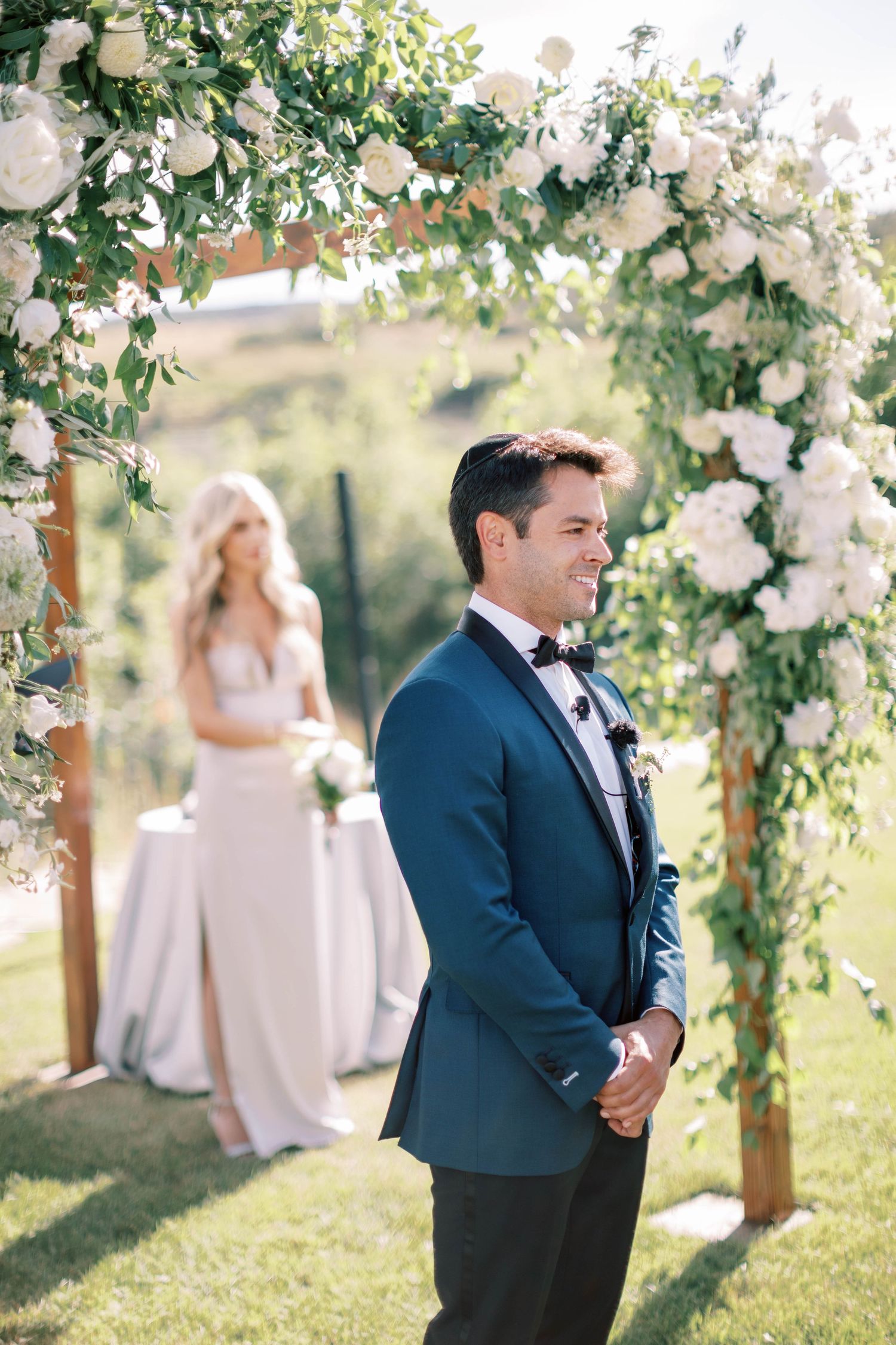 Wedding ceremony arch decorated with white roses and greenery in a garden setting.