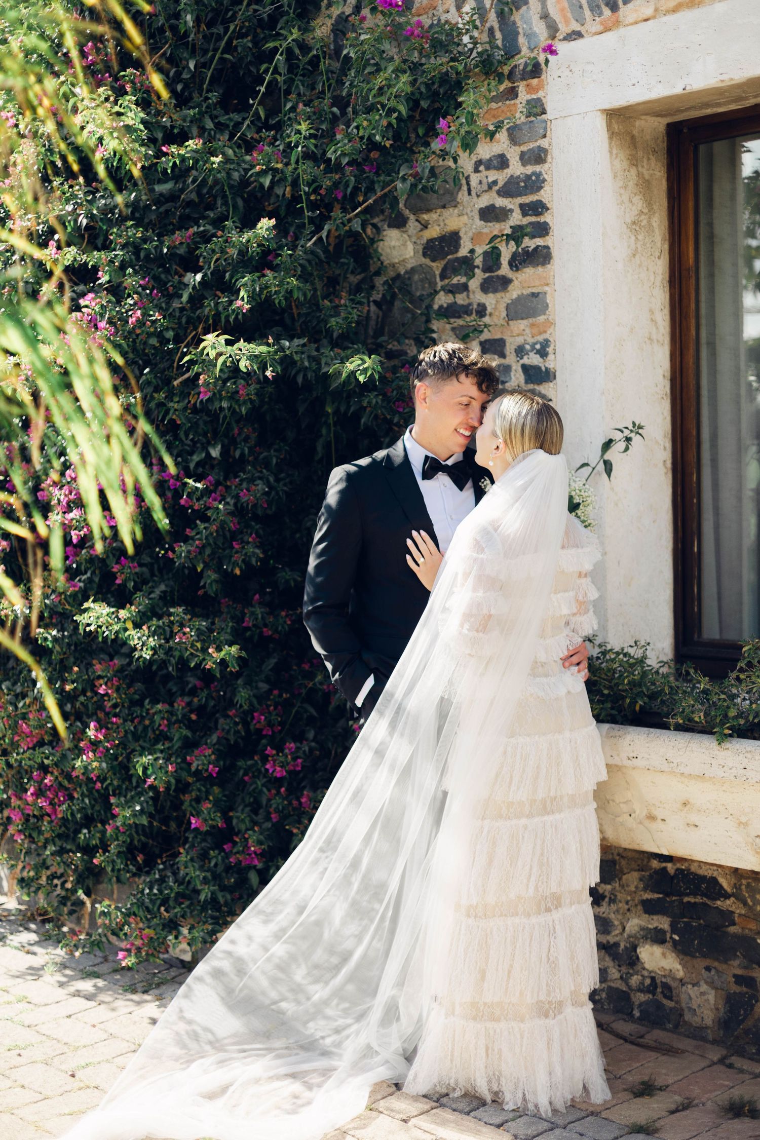 Wedding couple sharing intimate moment against stone wall with flowering vines at castello della castellucia in rome italy.