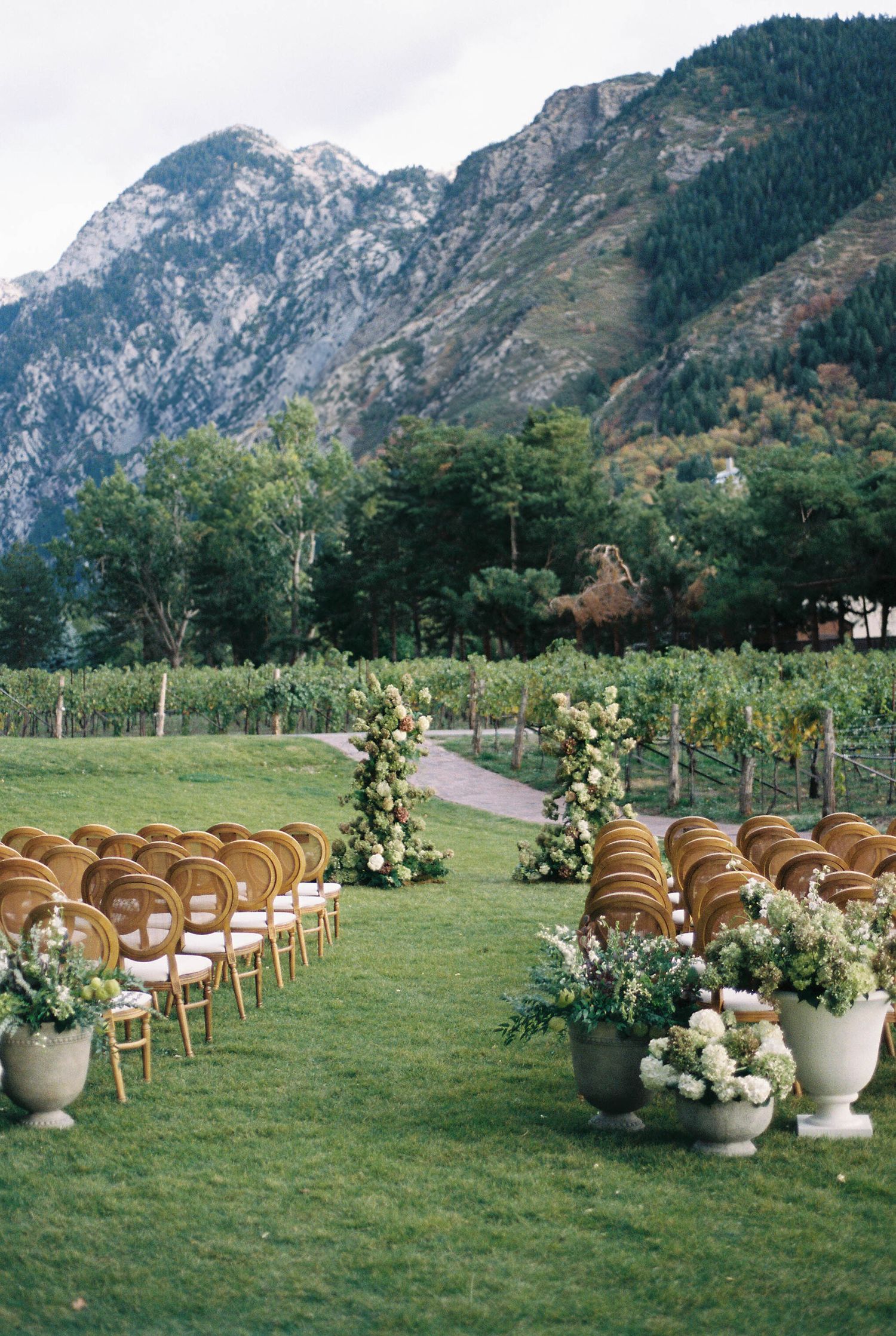 Mountain vineyard wedding ceremony setup with flower-adorned aisle and wooden chairs.