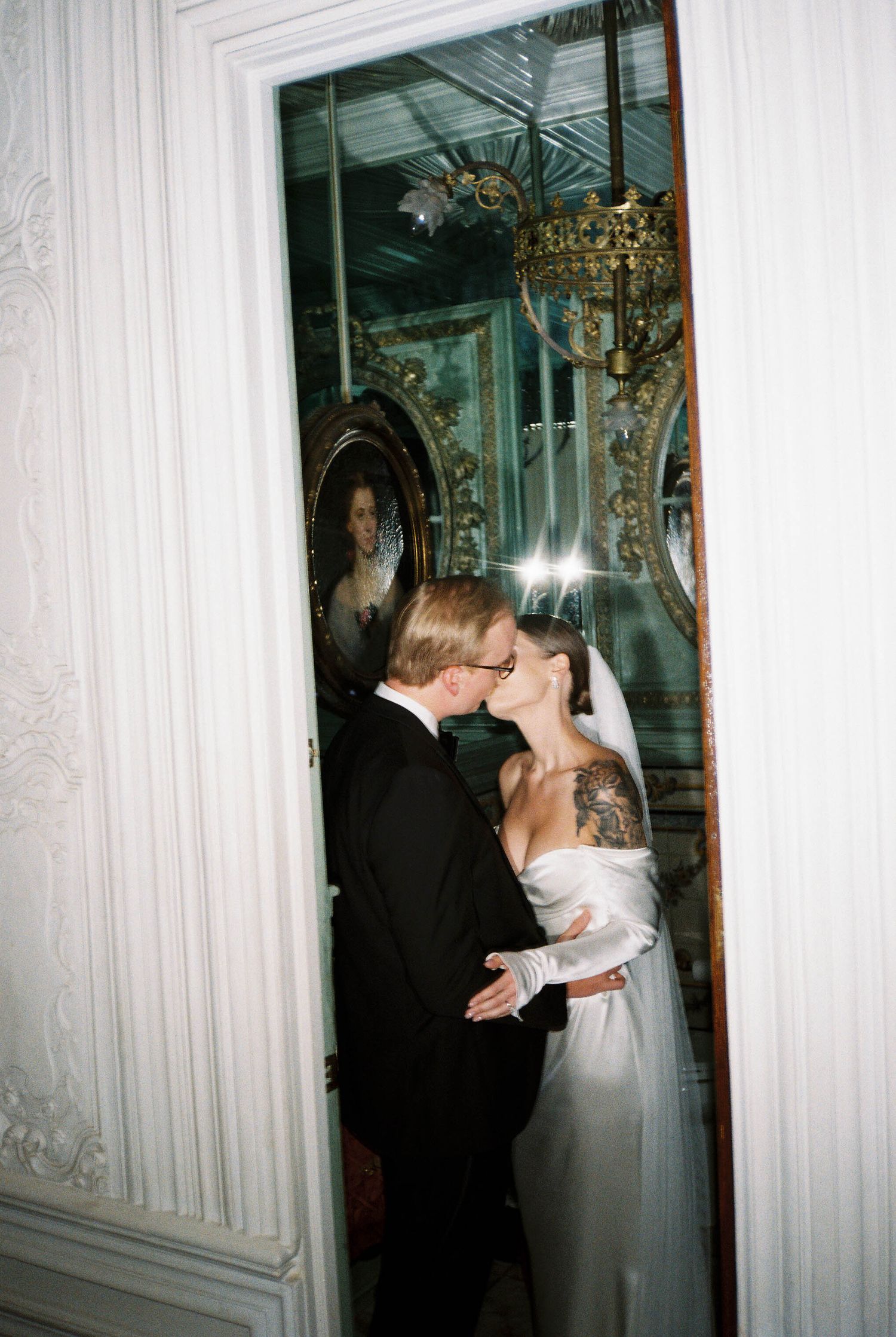 Couple sharing a kiss in an ornate hallway with mirrors and chandelier.