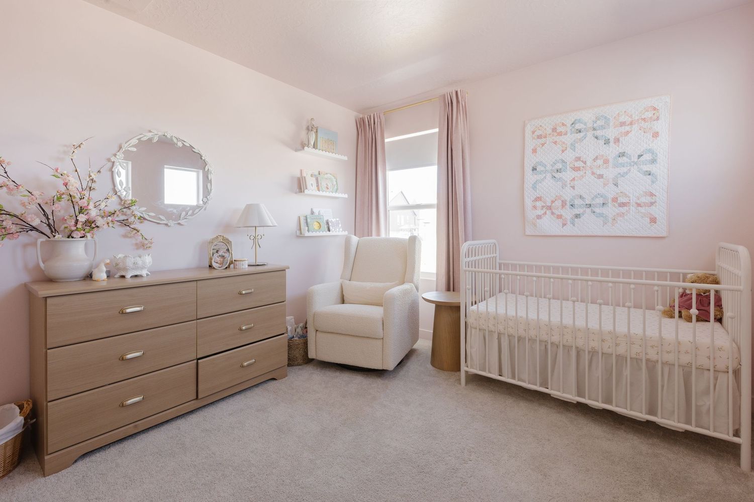 A serene nursery with light pink walls featuring a crib, dresser, and rocking chair.