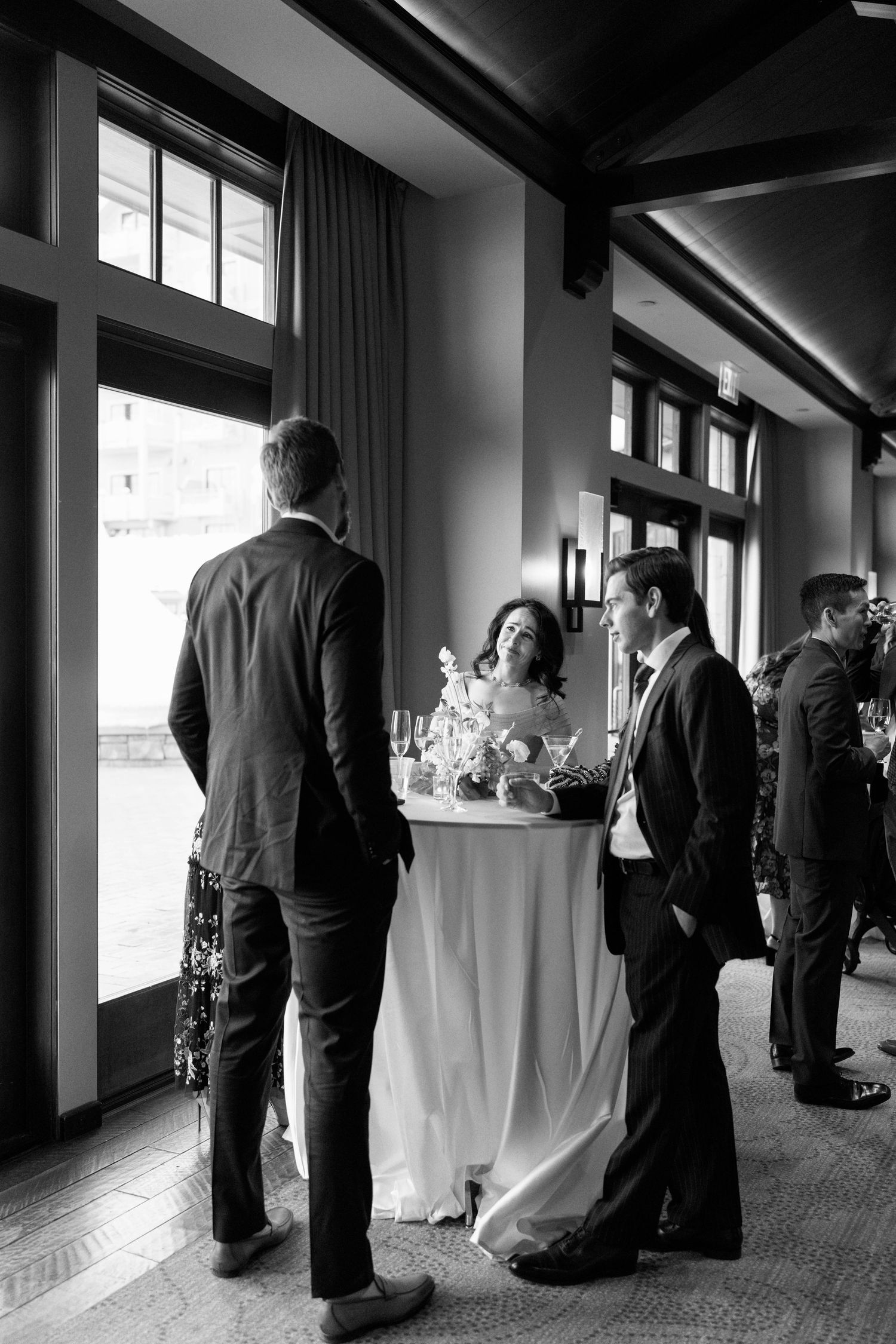 Black and white photo of guests mingling around a cocktail table at an upscale event.