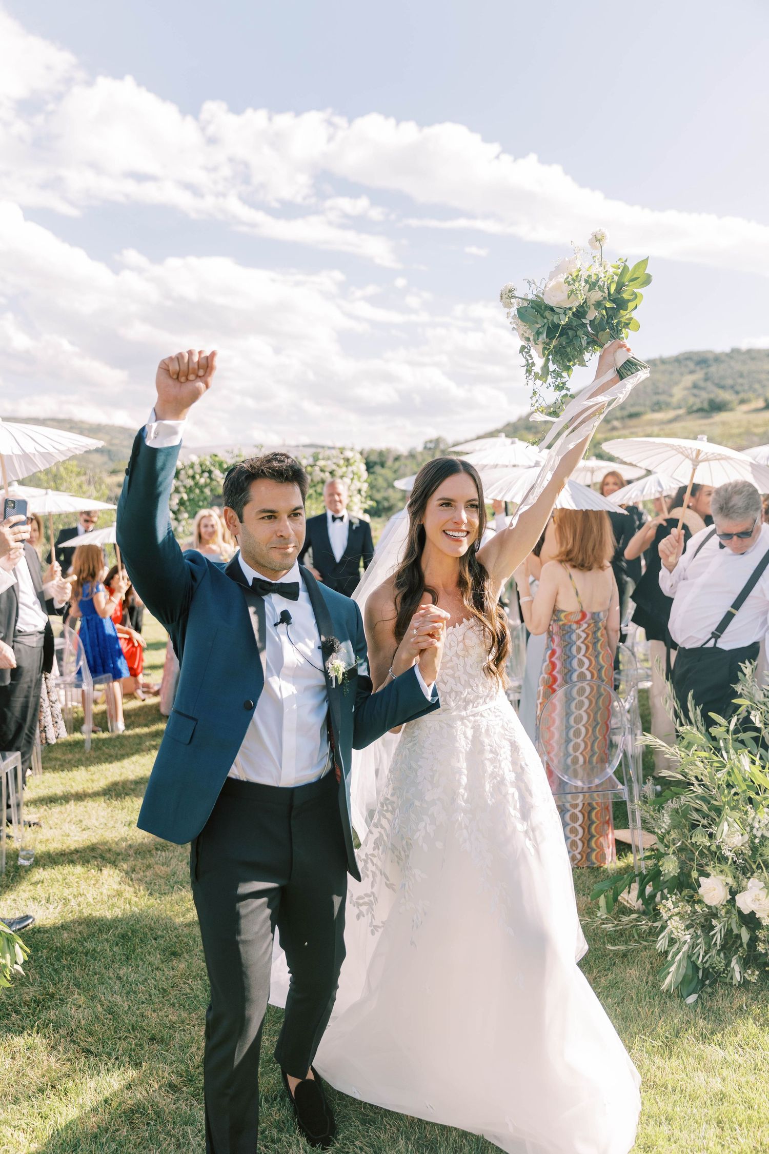 Newlyweds celebrating with raised arms at outdoor mountain wedding ceremony.