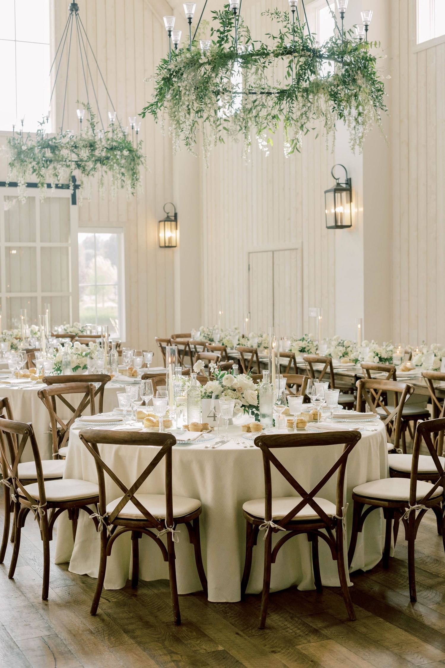 Elegant wedding reception venue with rustic chandeliers, cross-back chairs, and round tables.